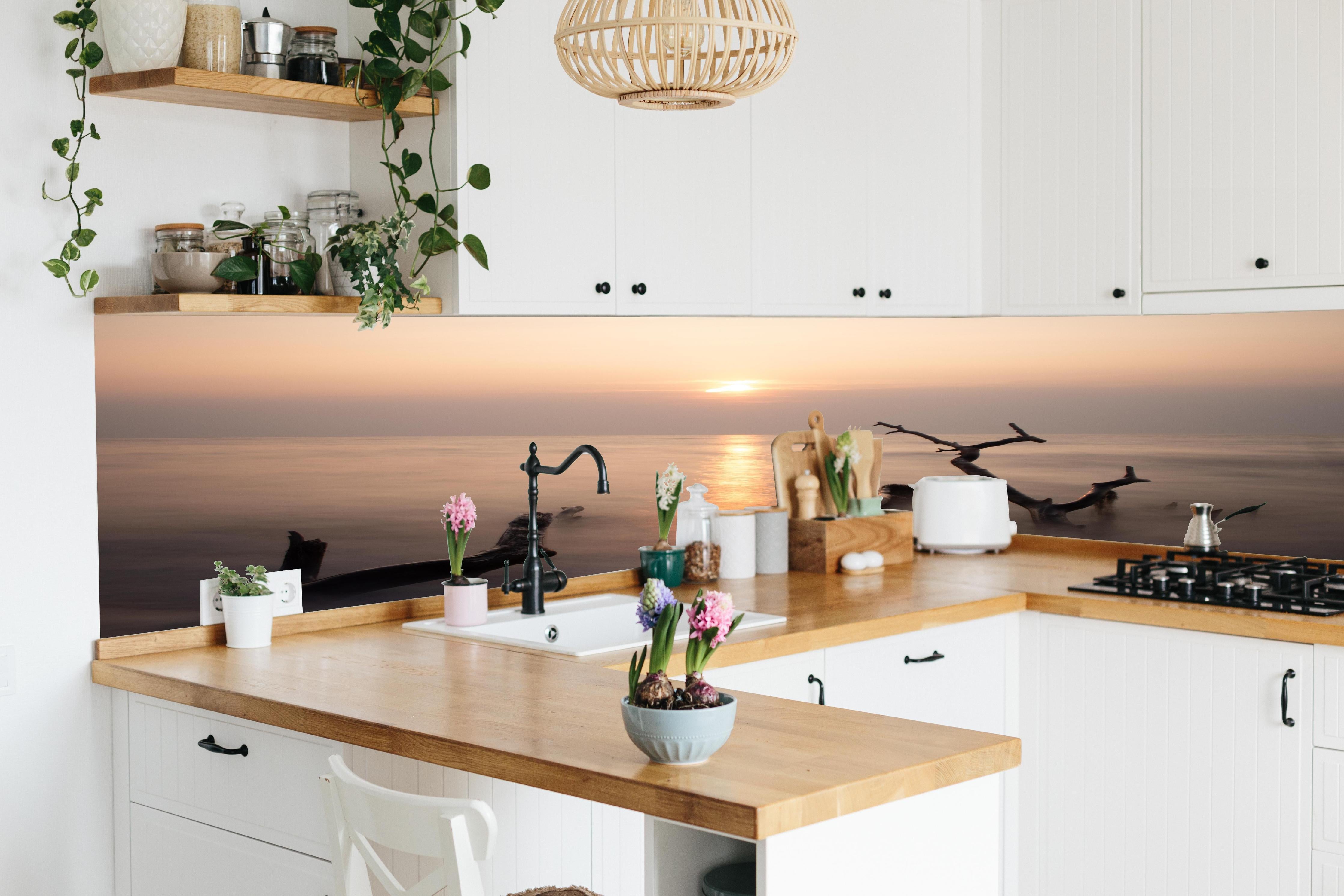 Küche - Stimmungsvoller Sonnenuntergangs-Strand hinter weißen Hochglanz-Küchenregalen und schwarzem Wasserhahn