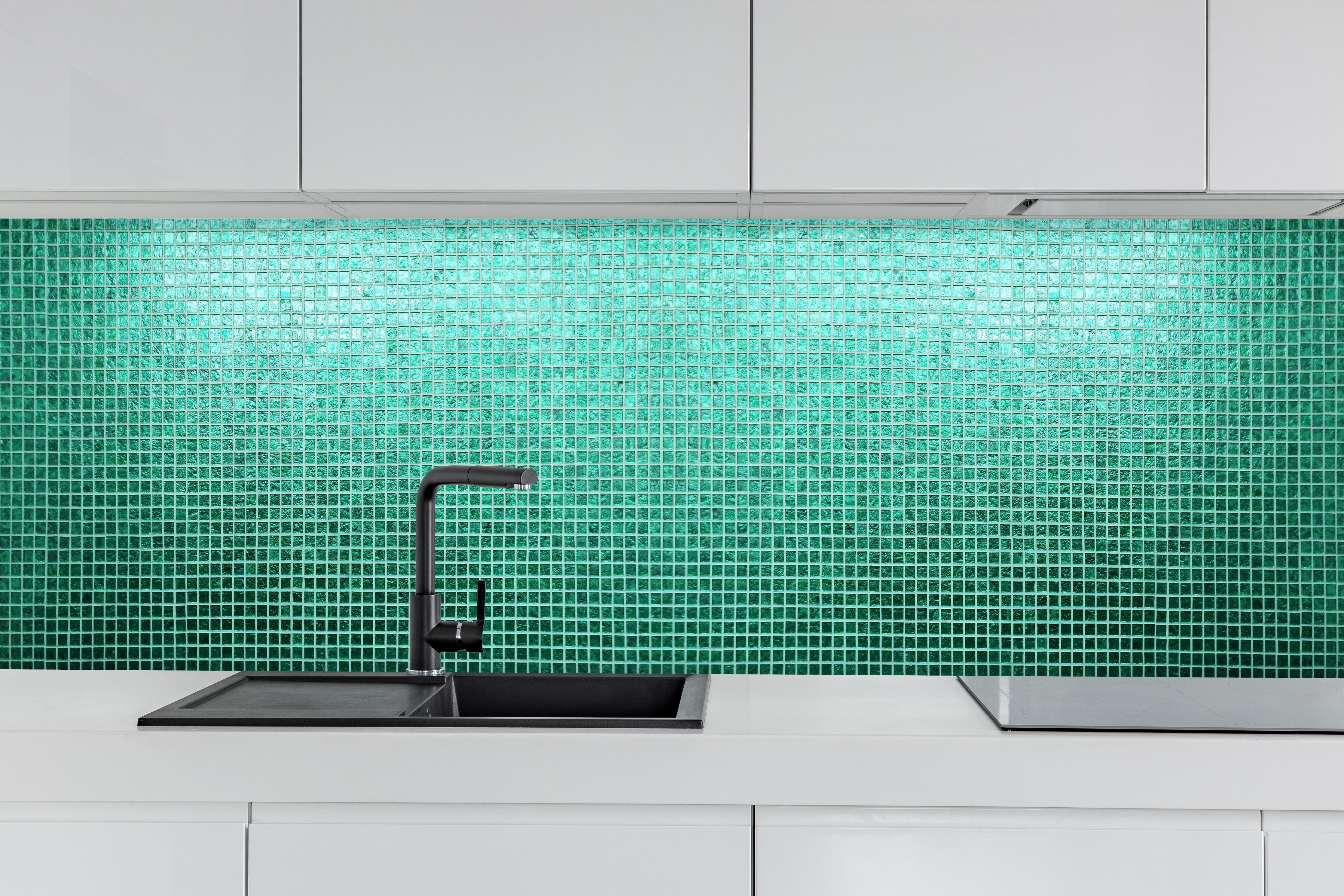 Küche - Strukturierte grüne Fliesenmosaik Textur hinter weißen Hochglanz-Küchenregalen und schwarzem Wasserhahn