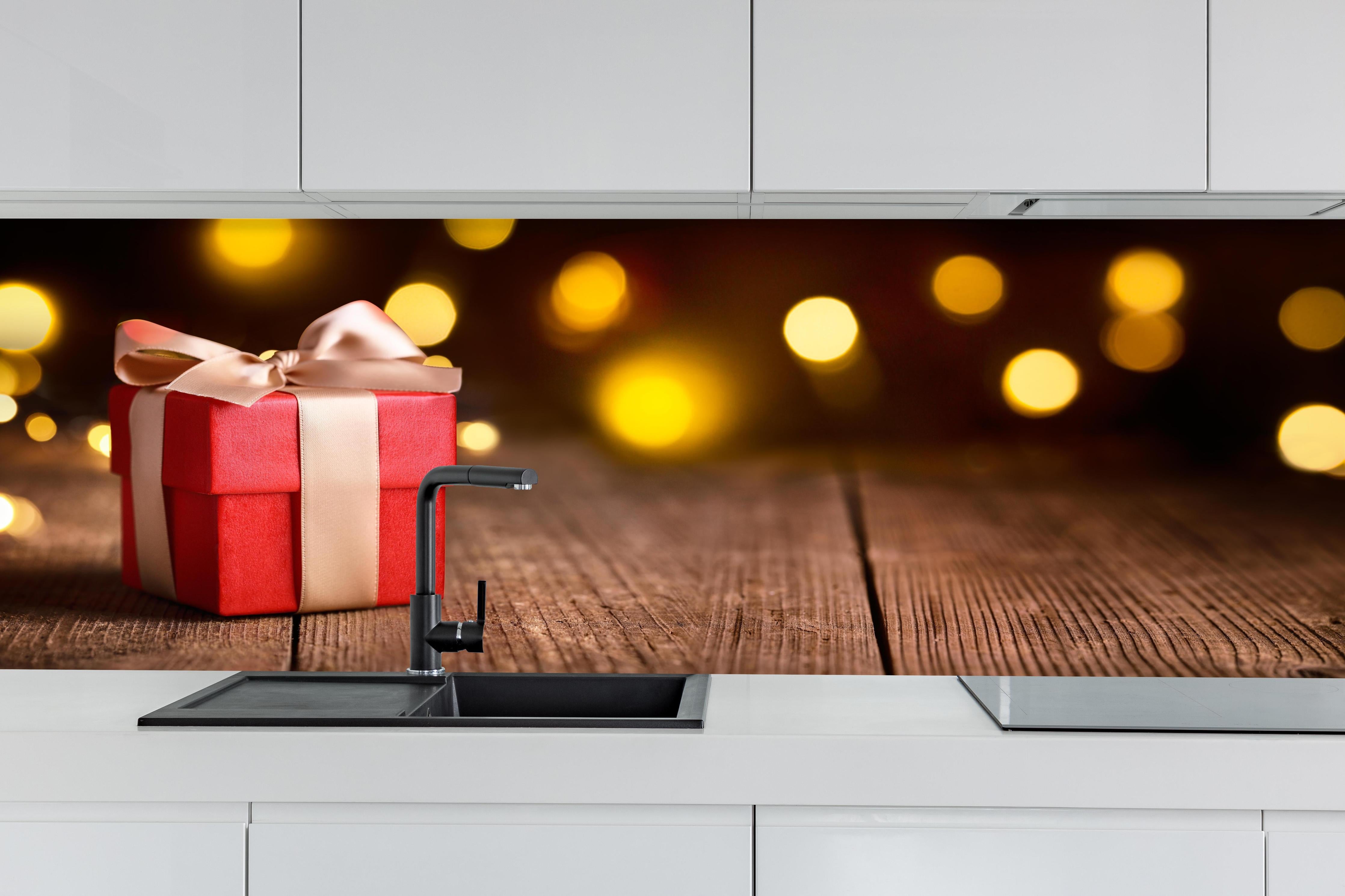 Küche - Weihnachtsgeschenk auf festlichem Hintergrund hinter weißen Hochglanz-Küchenregalen und schwarzem Wasserhahn