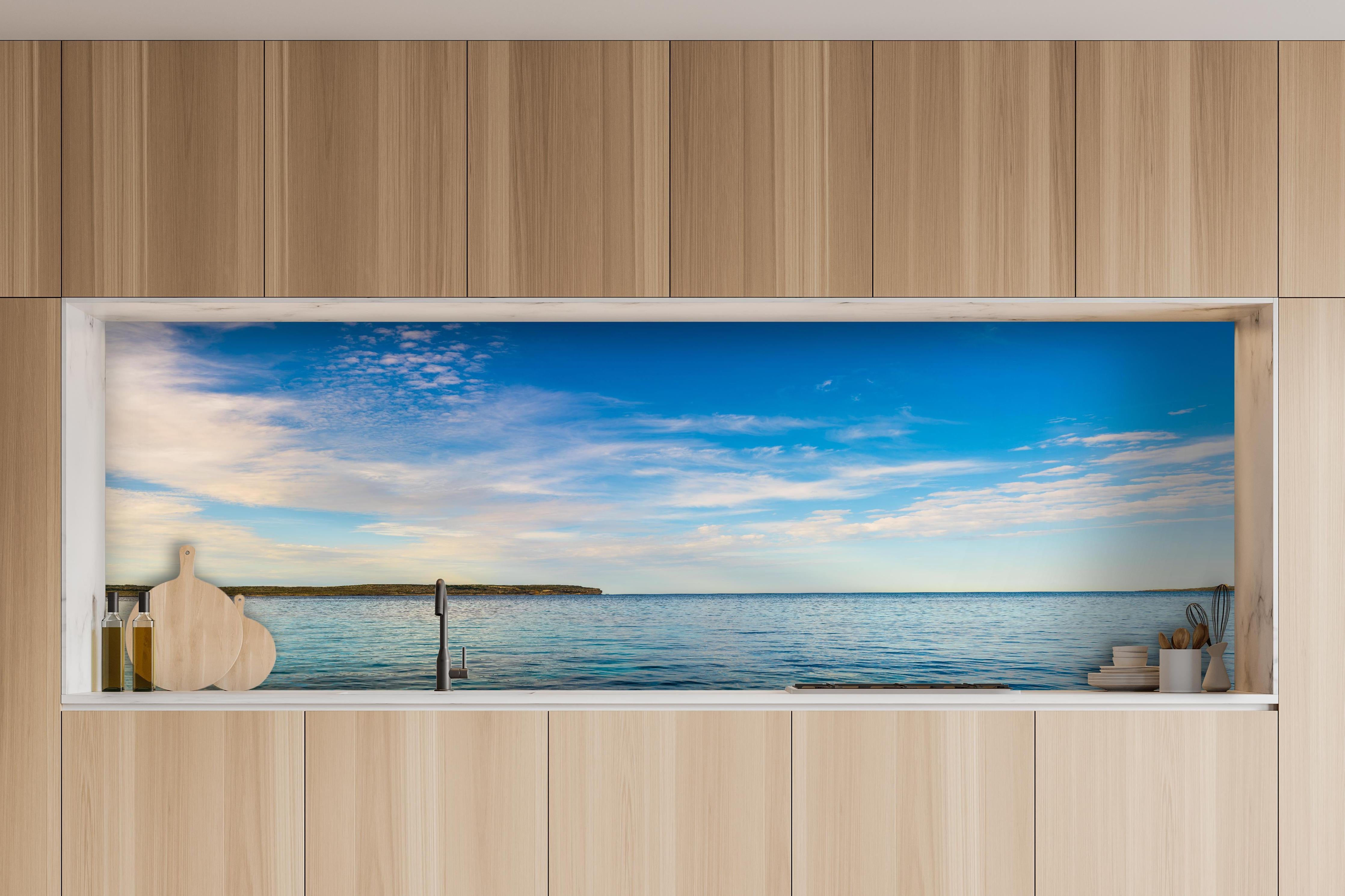 Küche - Weite und ruhige Meerelandschaft unter einem strahlend blauen Himmel hinter weißen Hochglanz-Küchenregalen und schwarzem Wasserhahn