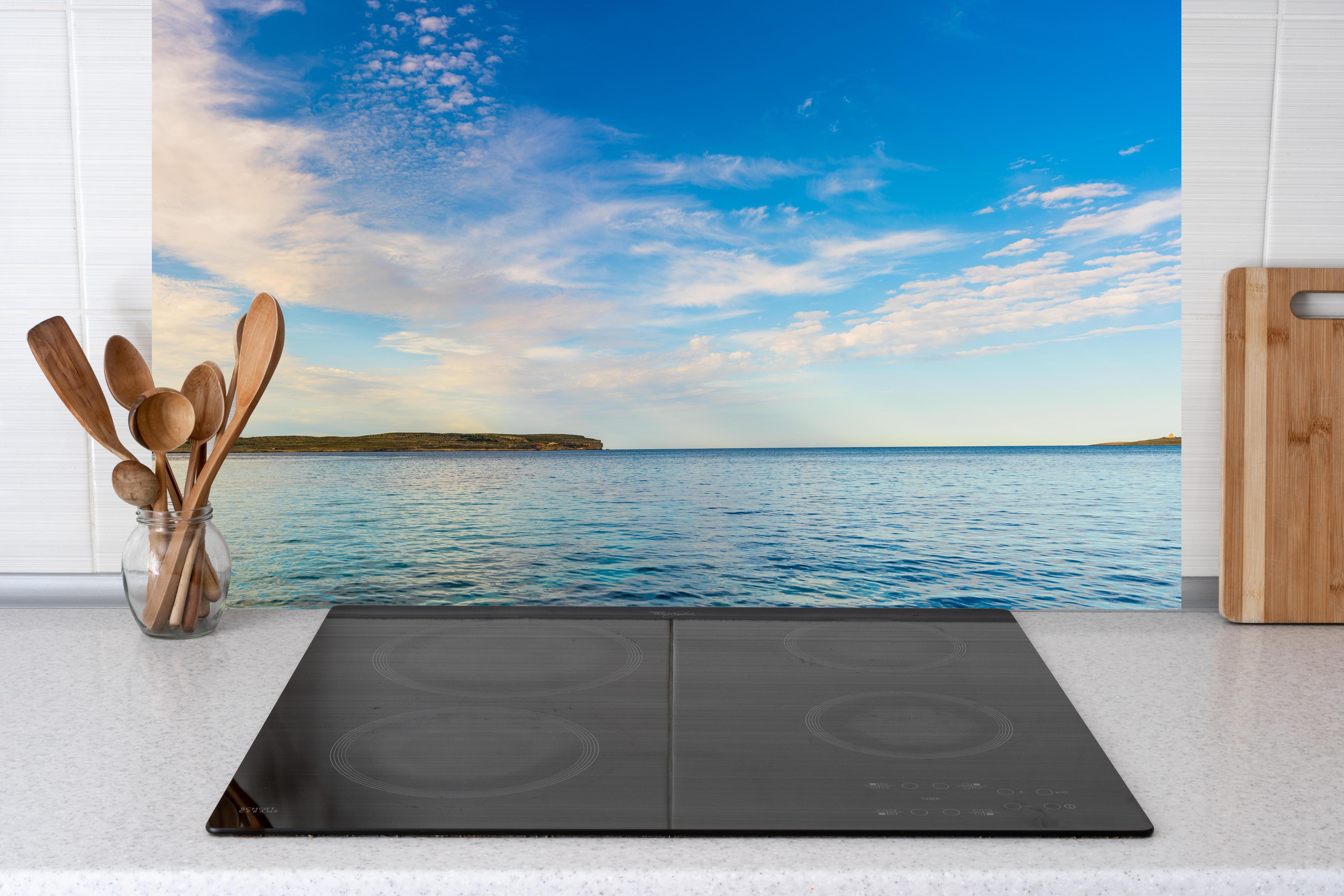 Küche - Weite und ruhige Meerelandschaft unter einem strahlend blauen Himmel hinter weißen Hochglanz-Küchenregalen und schwarzem Wasserhahn