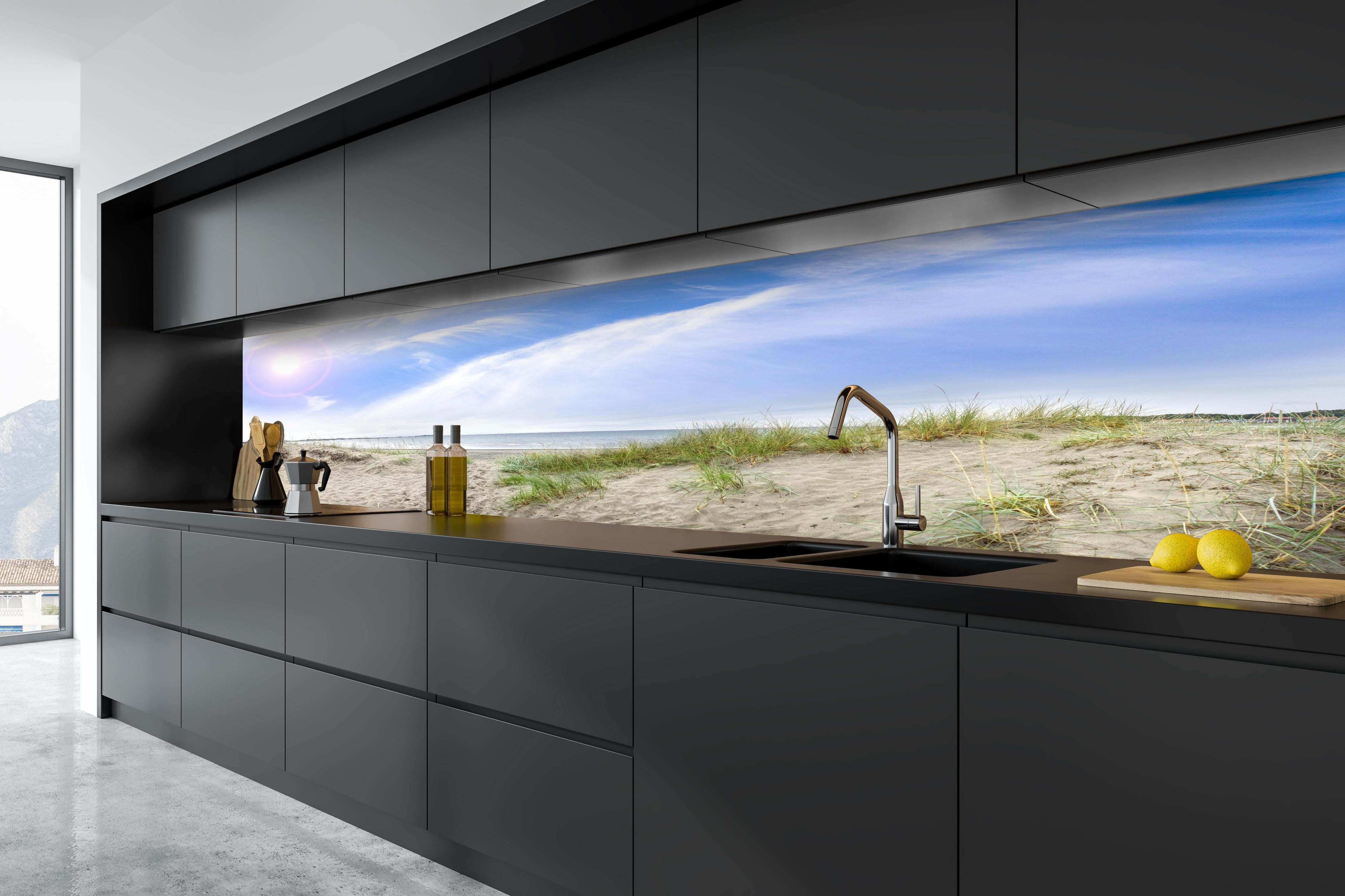 Küche - Weitläufige Strandlandschaft mit sanften Dünen, Himmel und ruhigem Wasser hinter weißen Hochglanz-Küchenregalen und schwarzem Wasserhahn