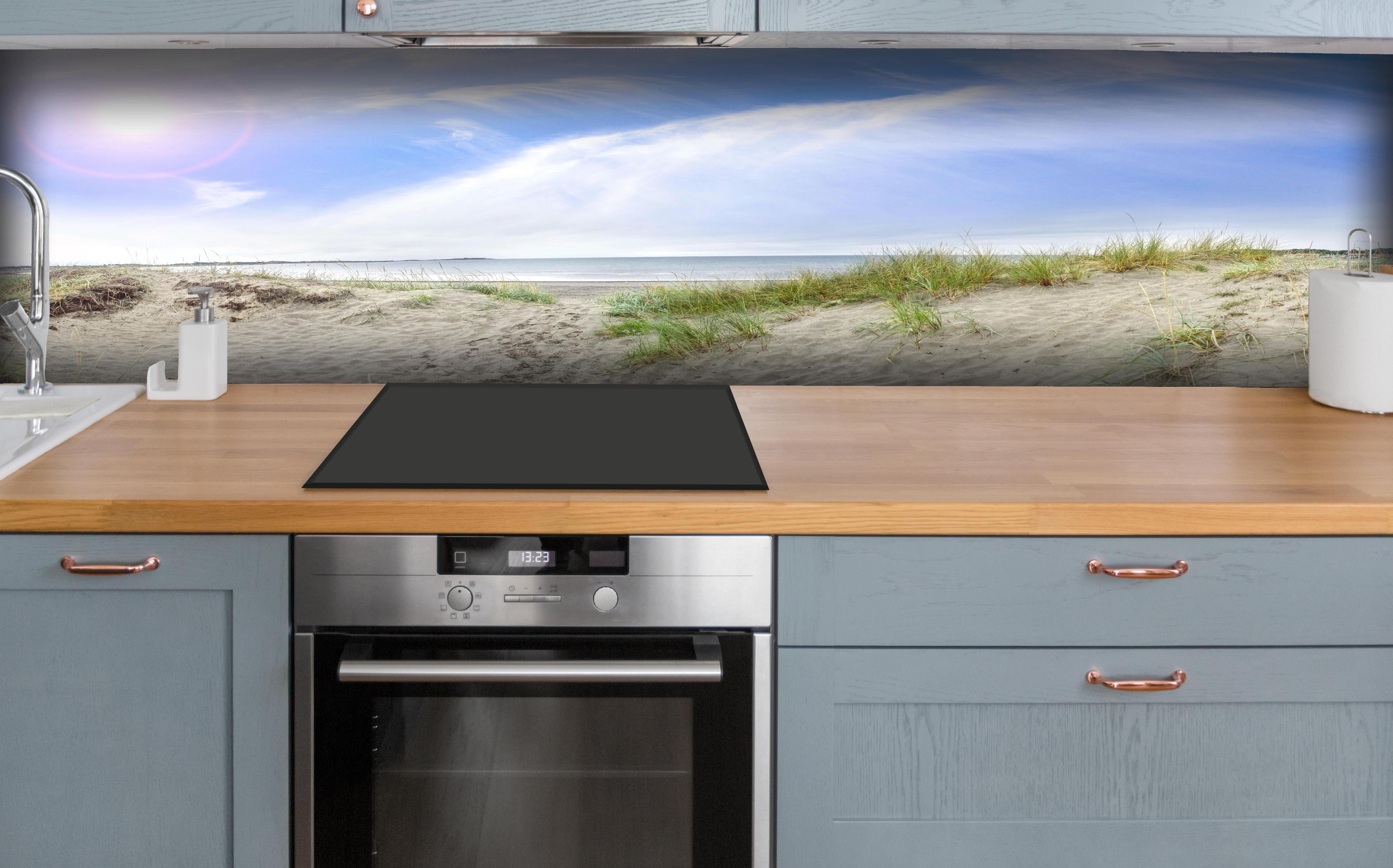 Küche - Weitläufige Strandlandschaft mit sanften Dünen, Himmel und ruhigem Wasser hinter weißen Hochglanz-Küchenregalen und schwarzem Wasserhahn