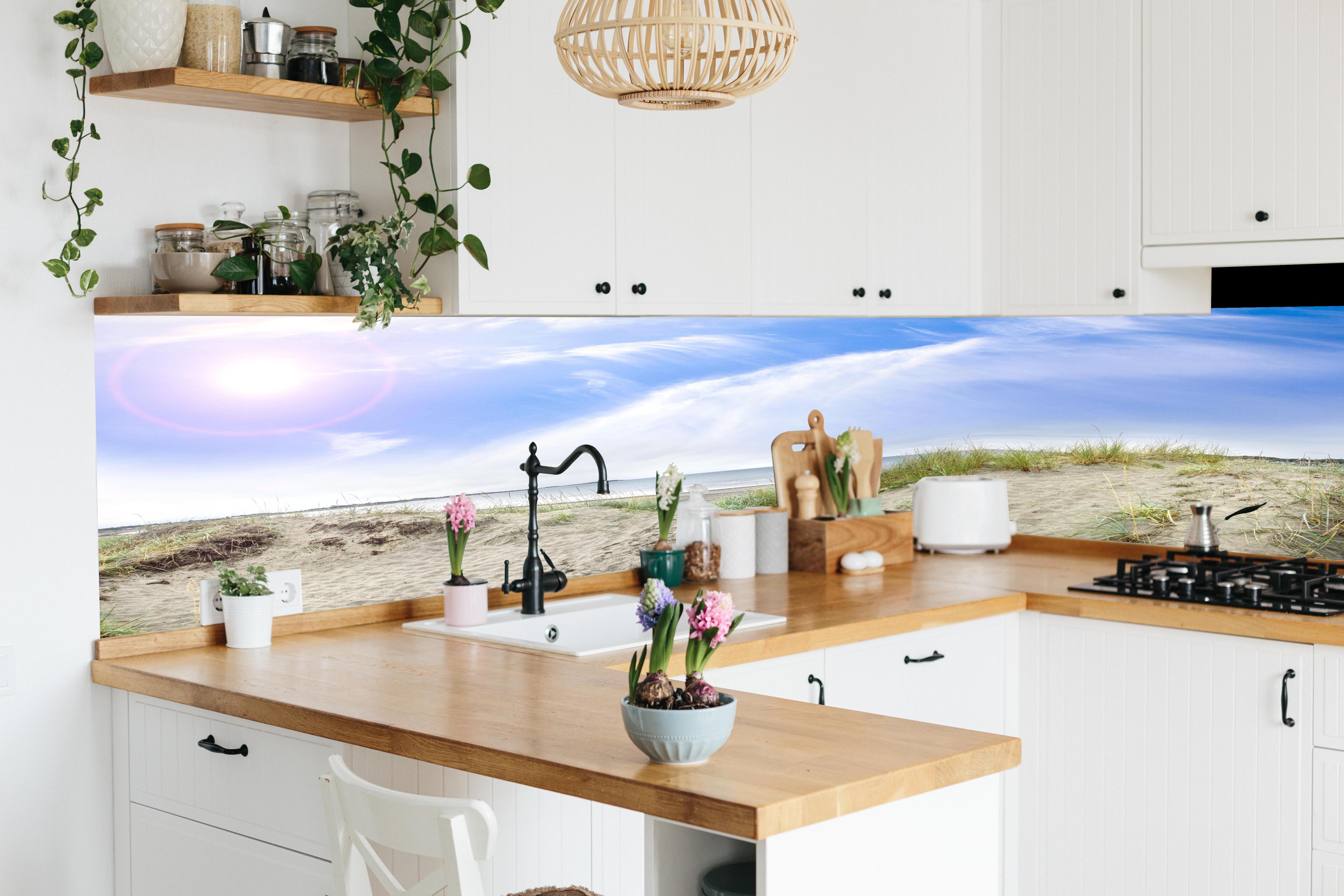 Küche - Weitläufige Strandlandschaft mit sanften Dünen, Himmel und ruhigem Wasser hinter weißen Hochglanz-Küchenregalen und schwarzem Wasserhahn