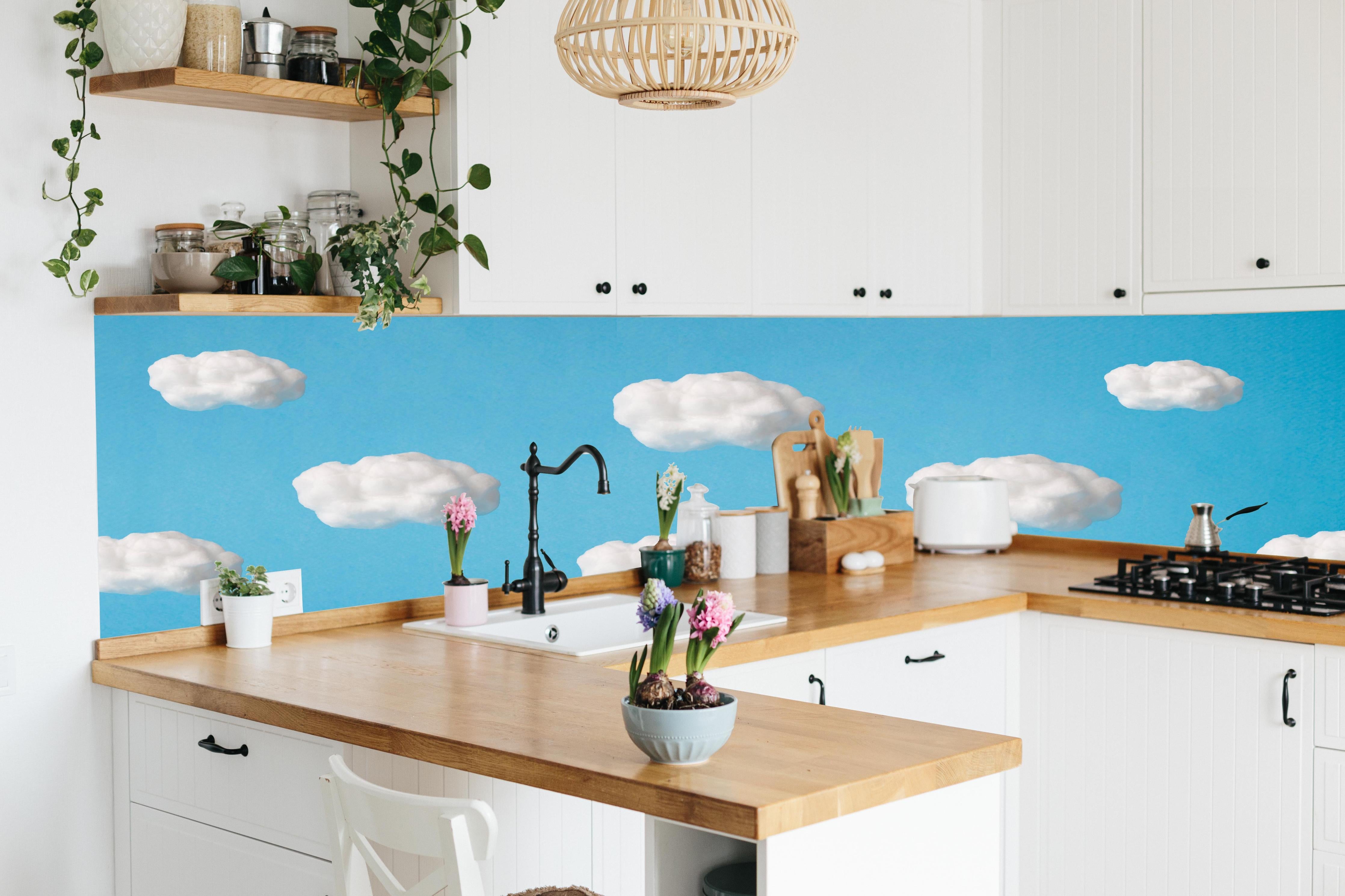 Küche - Wolke aus Watte auf himmelblauem Hintergrund hinter weißen Hochglanz-Küchenregalen und schwarzem Wasserhahn