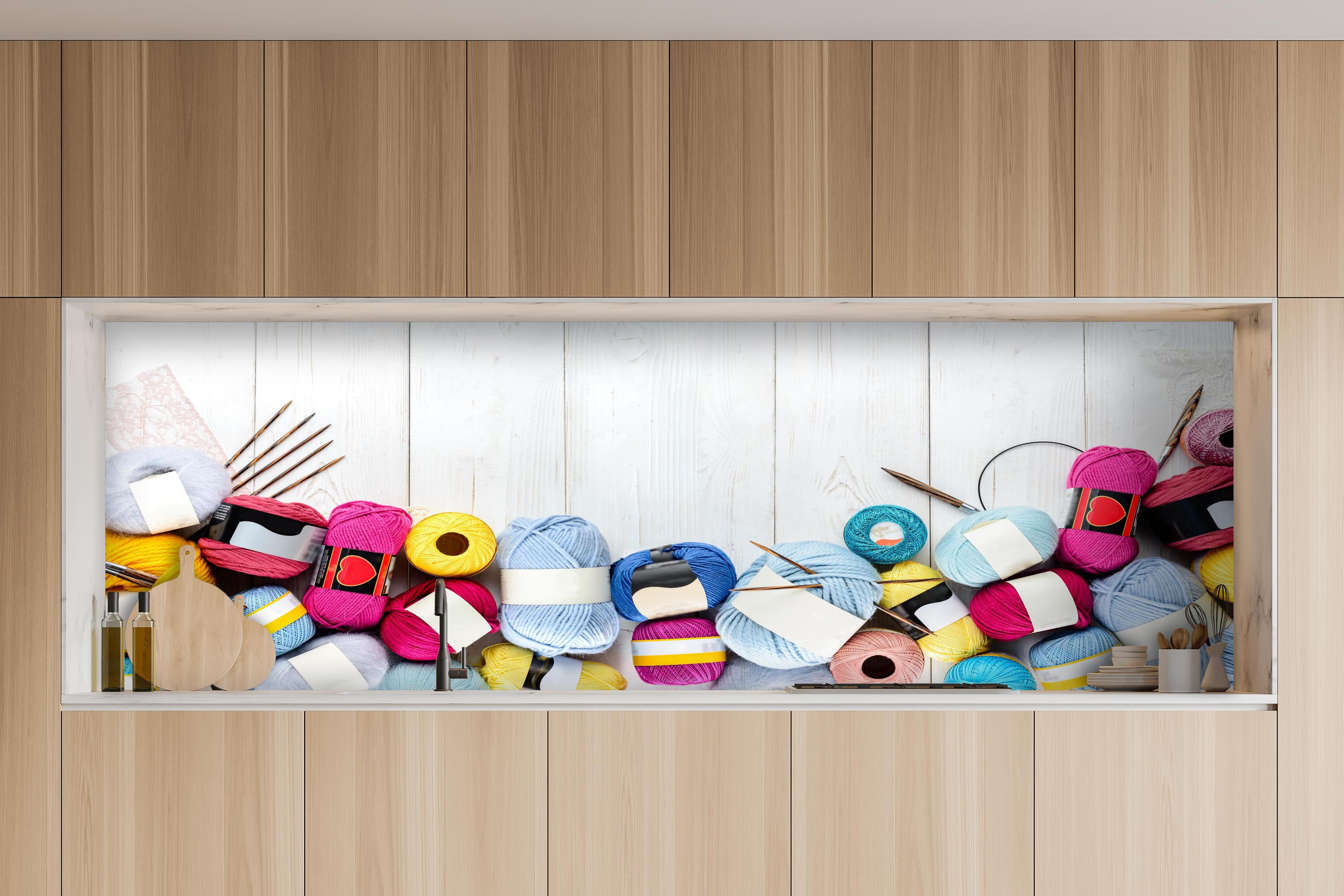 Küche - Wolle und Stricknadeln auf Holzhintergrund hinter weißen Hochglanz-Küchenregalen und schwarzem Wasserhahn