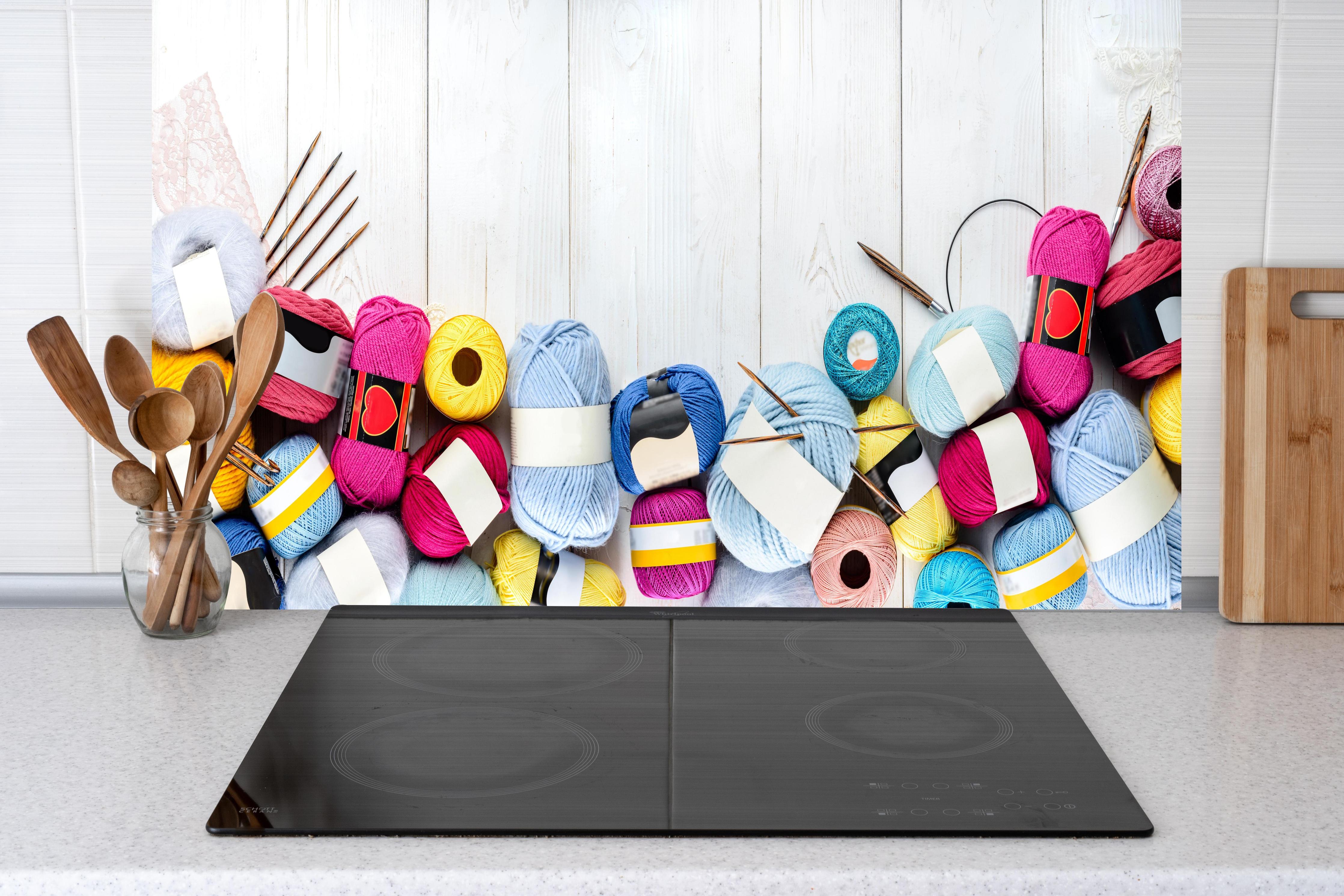 Küche - Wolle und Stricknadeln auf Holzhintergrund hinter weißen Hochglanz-Küchenregalen und schwarzem Wasserhahn