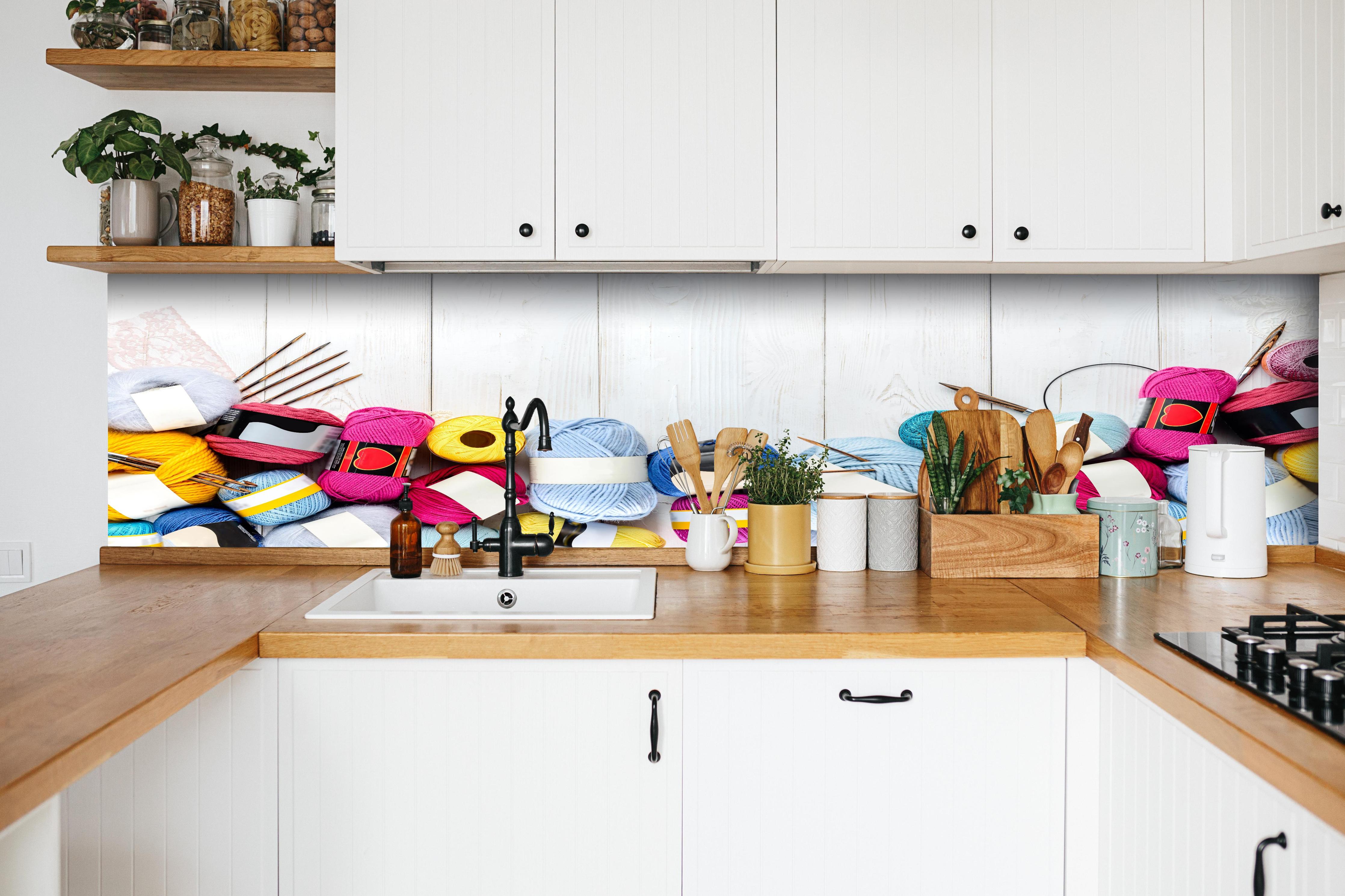 Küche - Wolle und Stricknadeln auf Holzhintergrund hinter weißen Hochglanz-Küchenregalen und schwarzem Wasserhahn