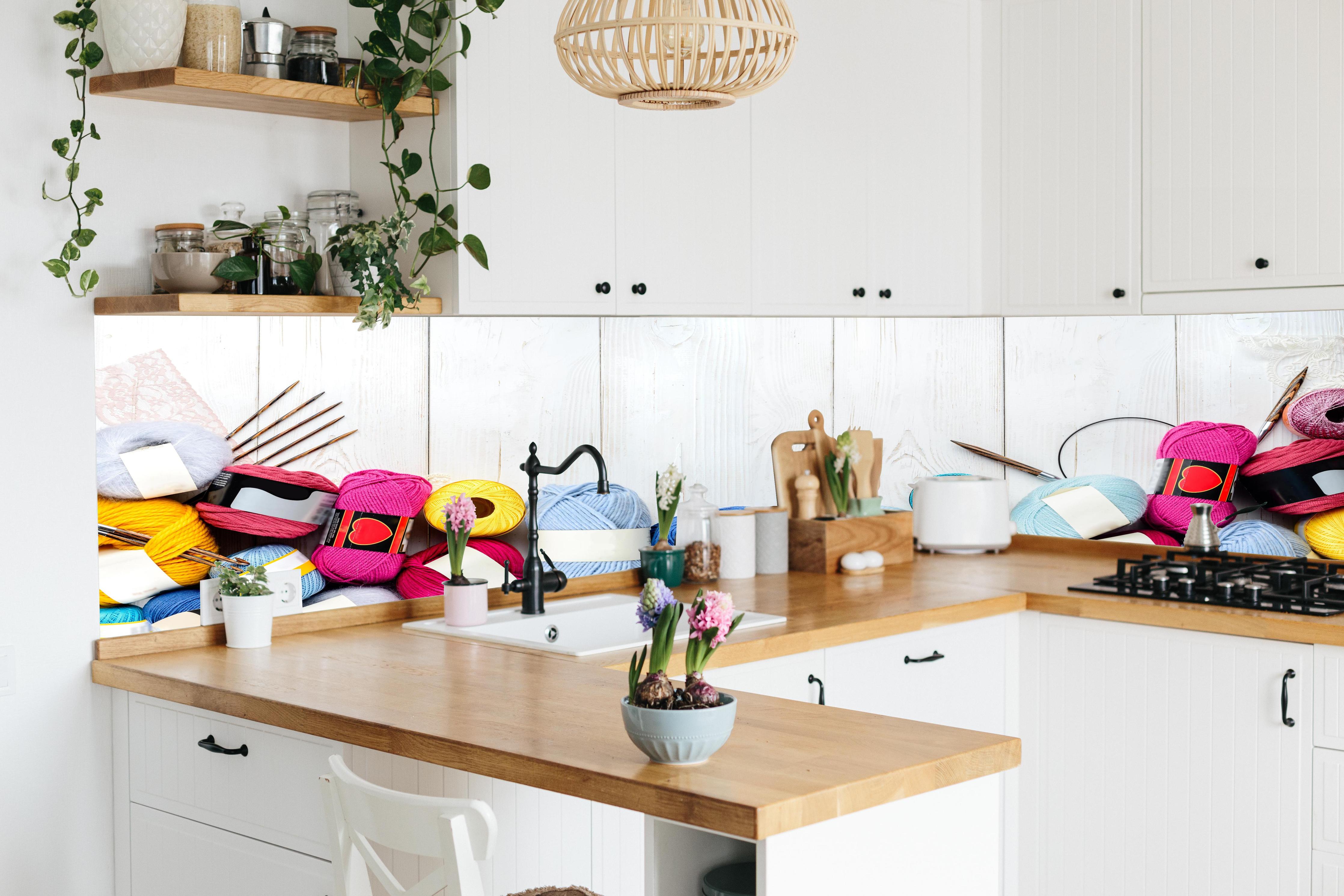 Küche - Wolle und Stricknadeln auf Holzhintergrund hinter weißen Hochglanz-Küchenregalen und schwarzem Wasserhahn