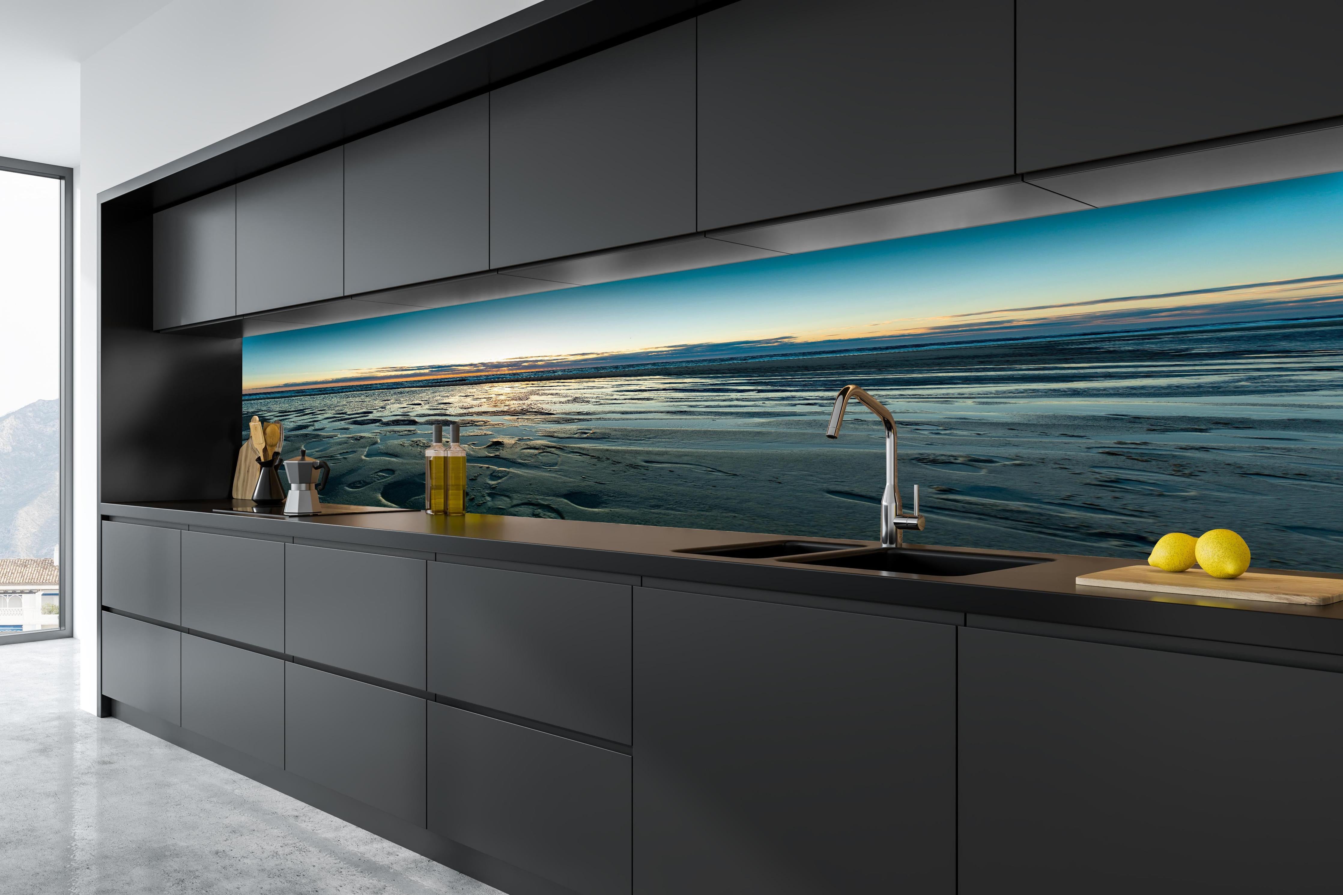 Küche - Wunderschöne blaue und orange Strandlandschaft mit Sonnenuntergang hinter weißen Hochglanz-Küchenregalen und schwarzem Wasserhahn