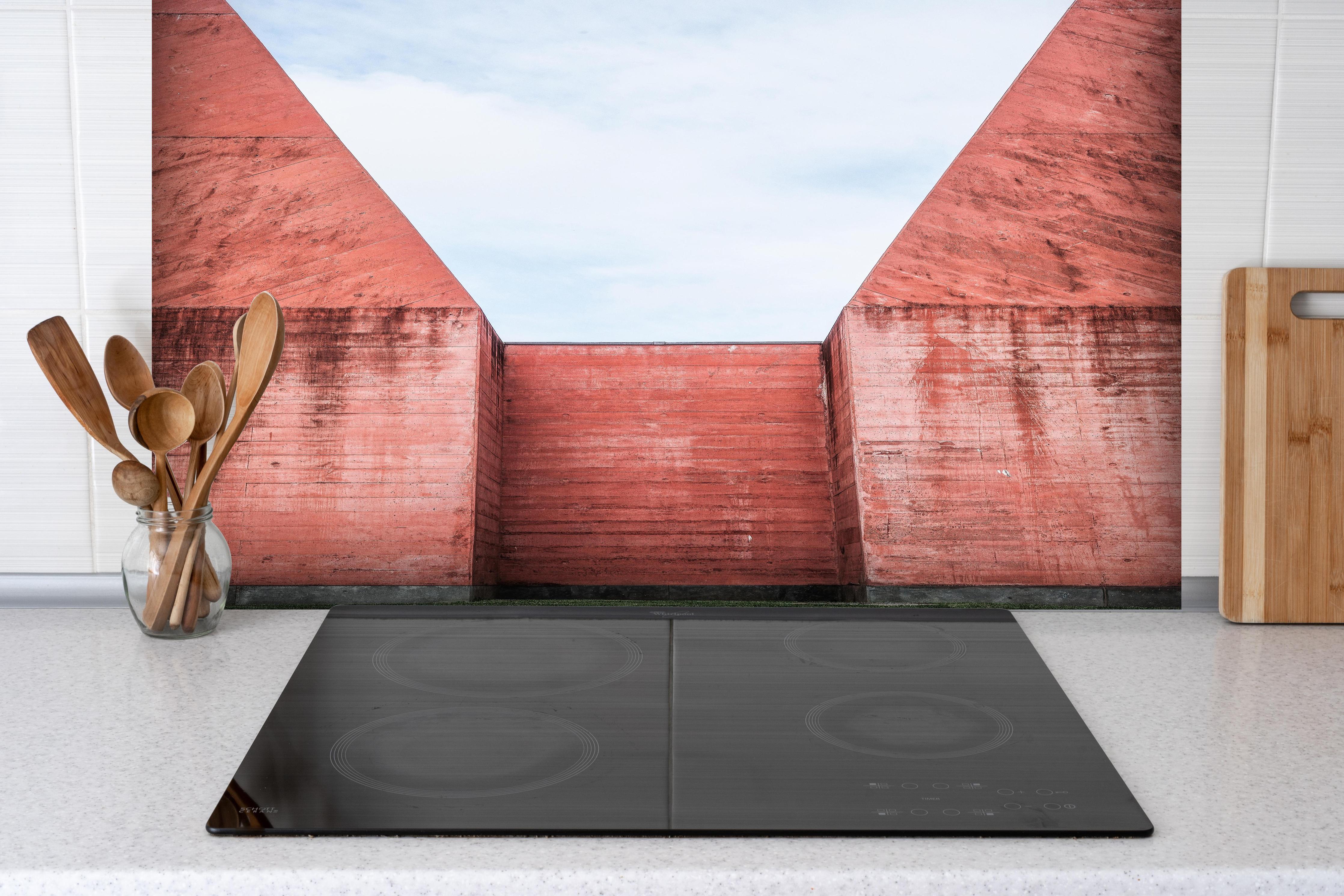 Spritzschutz - Abstrakte Architektur in Marsrot hinter einem Cerankochfeld zwischen Holz-Kochutensilien
