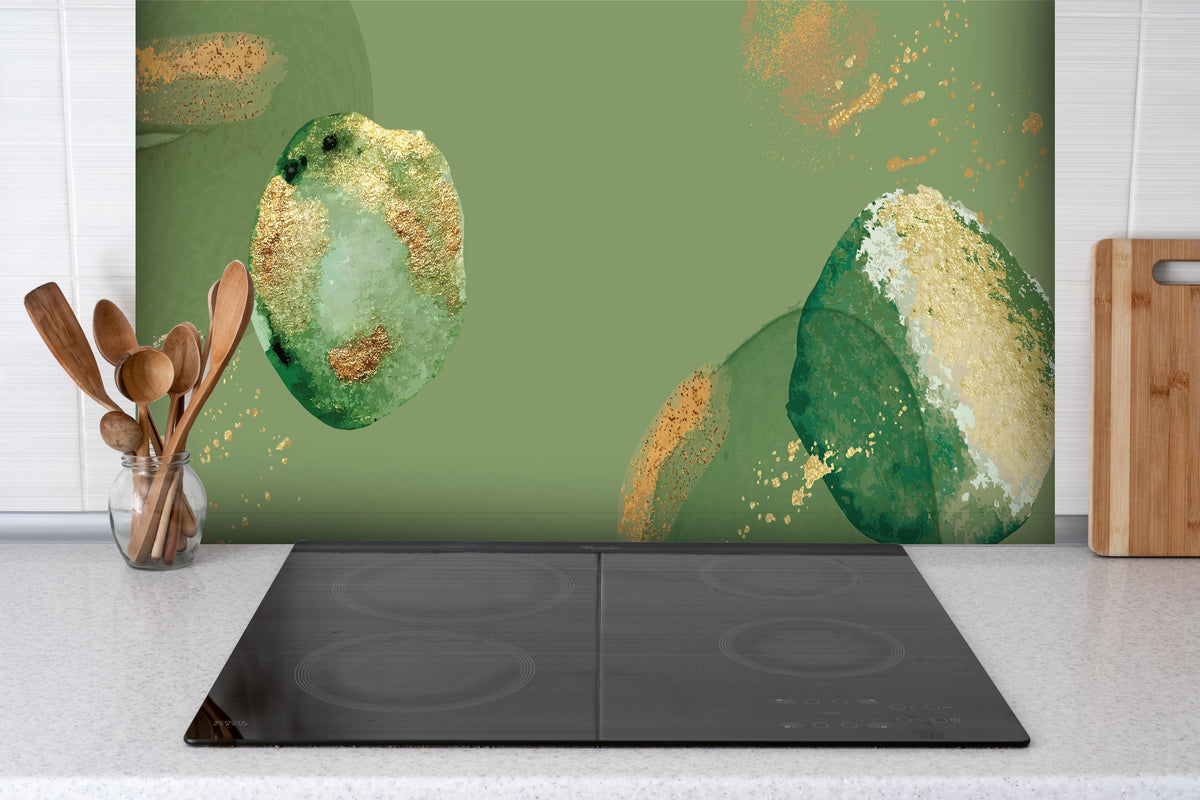 Spritzschutz - Abstrakte Kunst in Grün und Goldtönen hinter einem Cerankochfeld zwischen Holz-Kochutensilien
