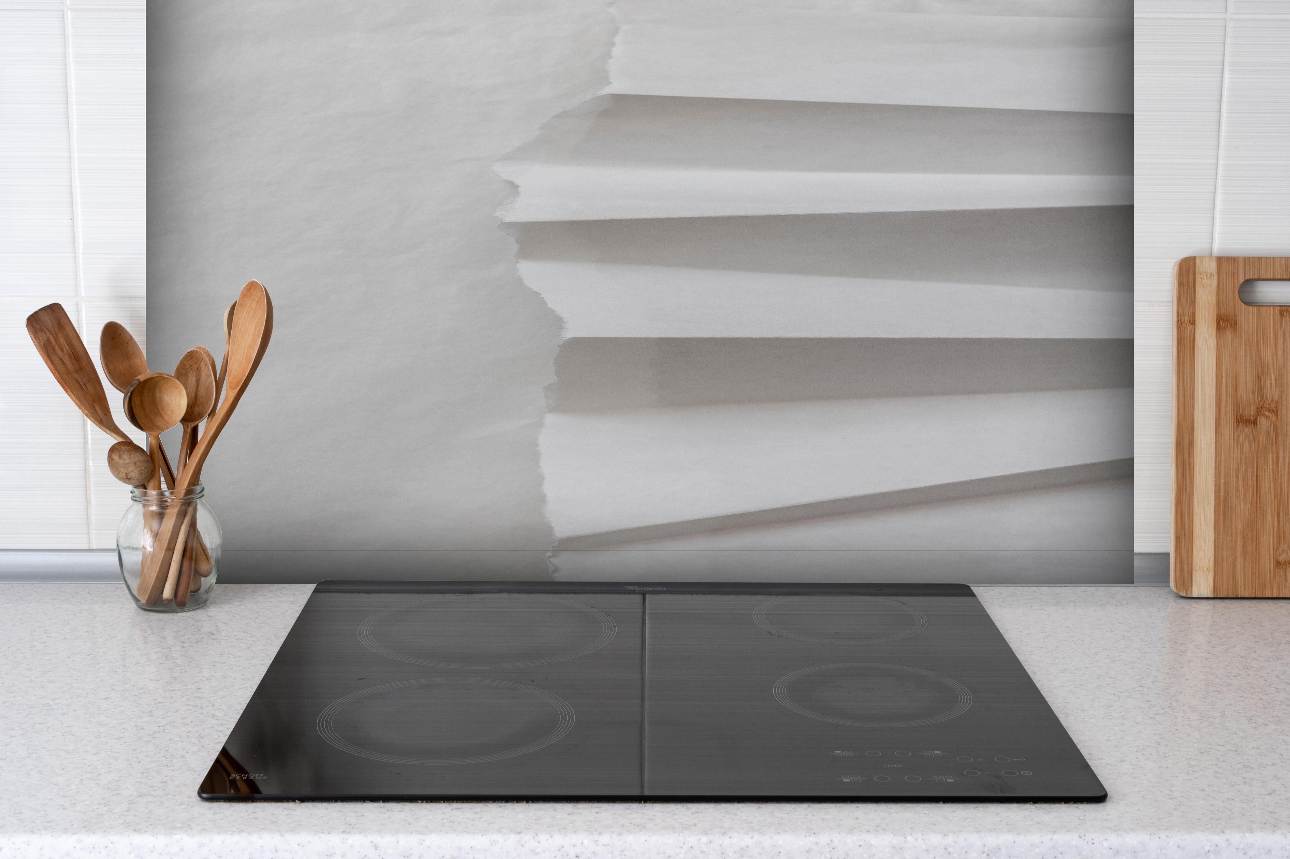 Spritzschutz - Abstrakte weiβe Papierkunst mit Grautönen hinter einem Cerankochfeld zwischen Holz-Kochutensilien
