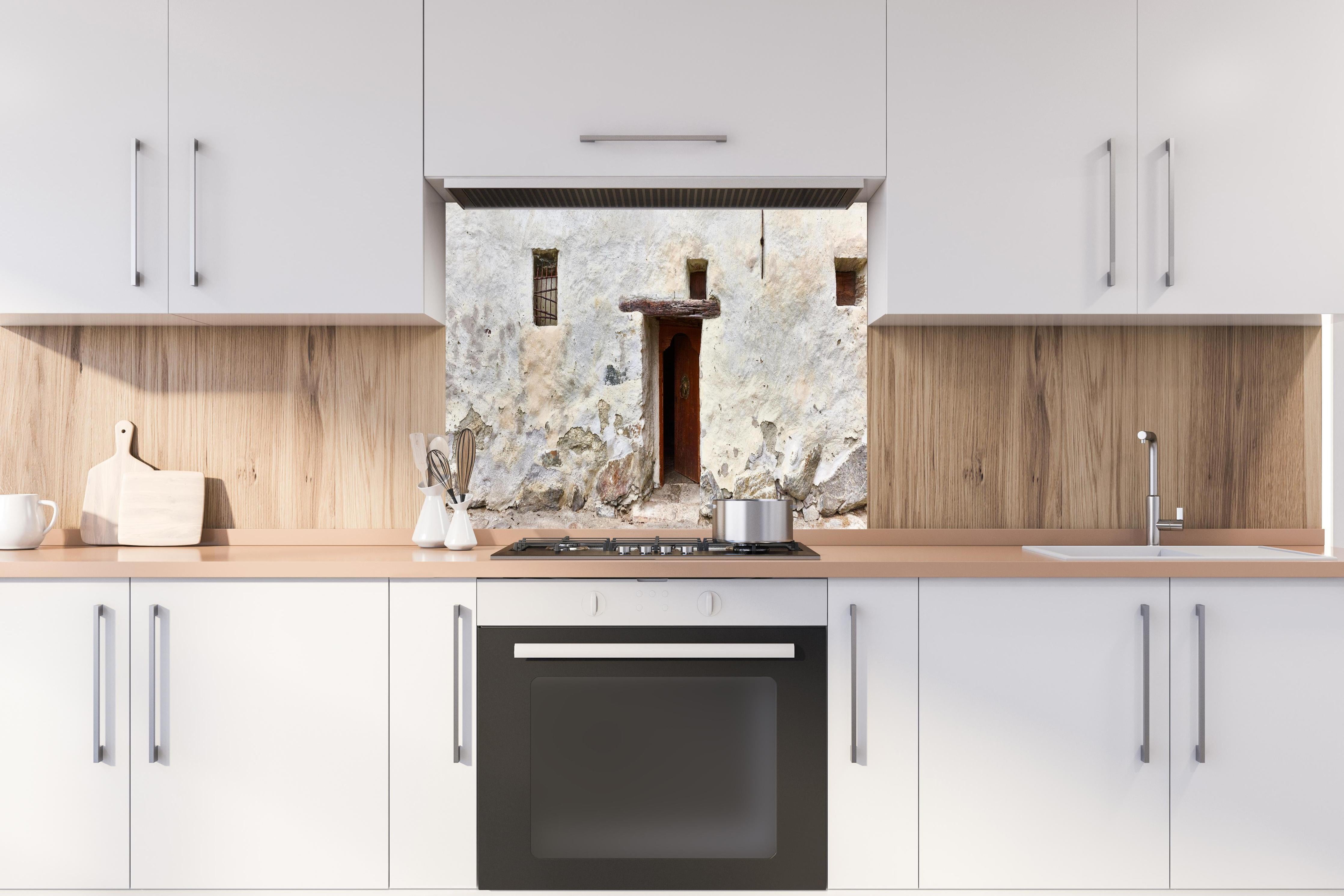 Spritzschutz - Alter Türeingang in Südtirol hinter einem Cerankochfeld zwischen Holz-Kochutensilien
