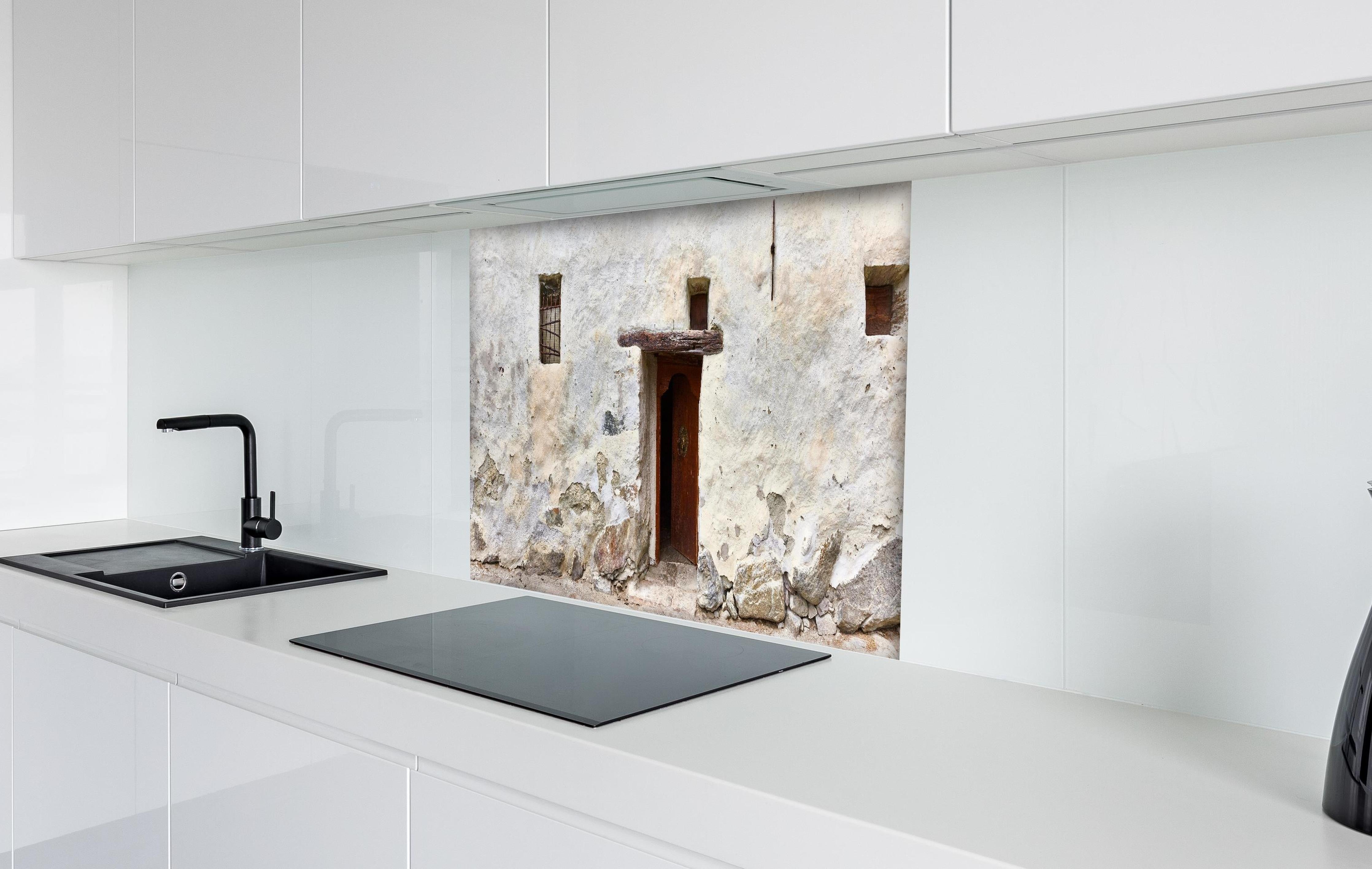 Spritzschutz - Alter Türeingang in Südtirol hinter einem Cerankochfeld zwischen Holz-Kochutensilien
