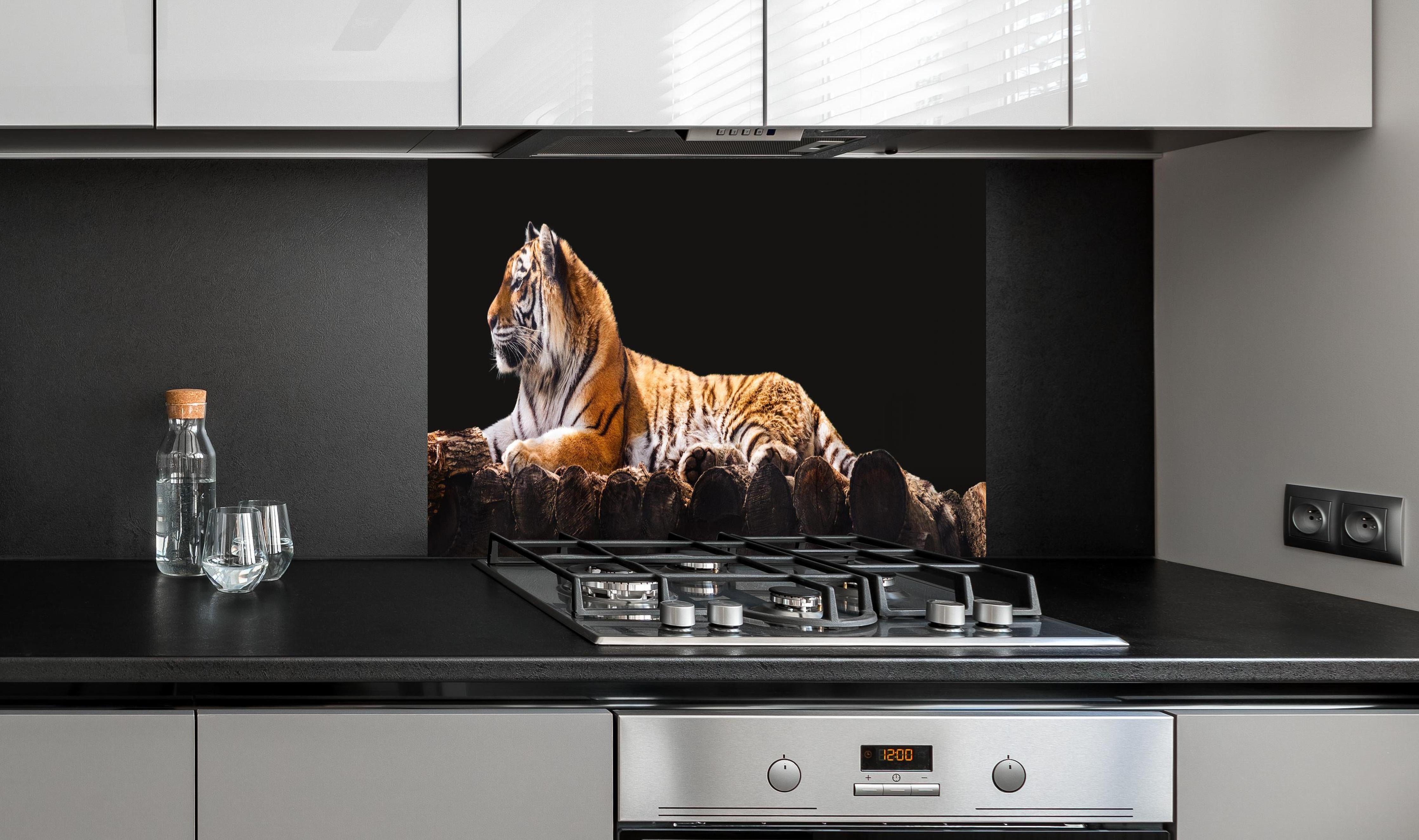 Spritzschutz - Amurtiger liegend auf Holzdeck mit Schwarzem Hintergrund hinter einem Cerankochfeld zwischen Holz-Kochutensilien
