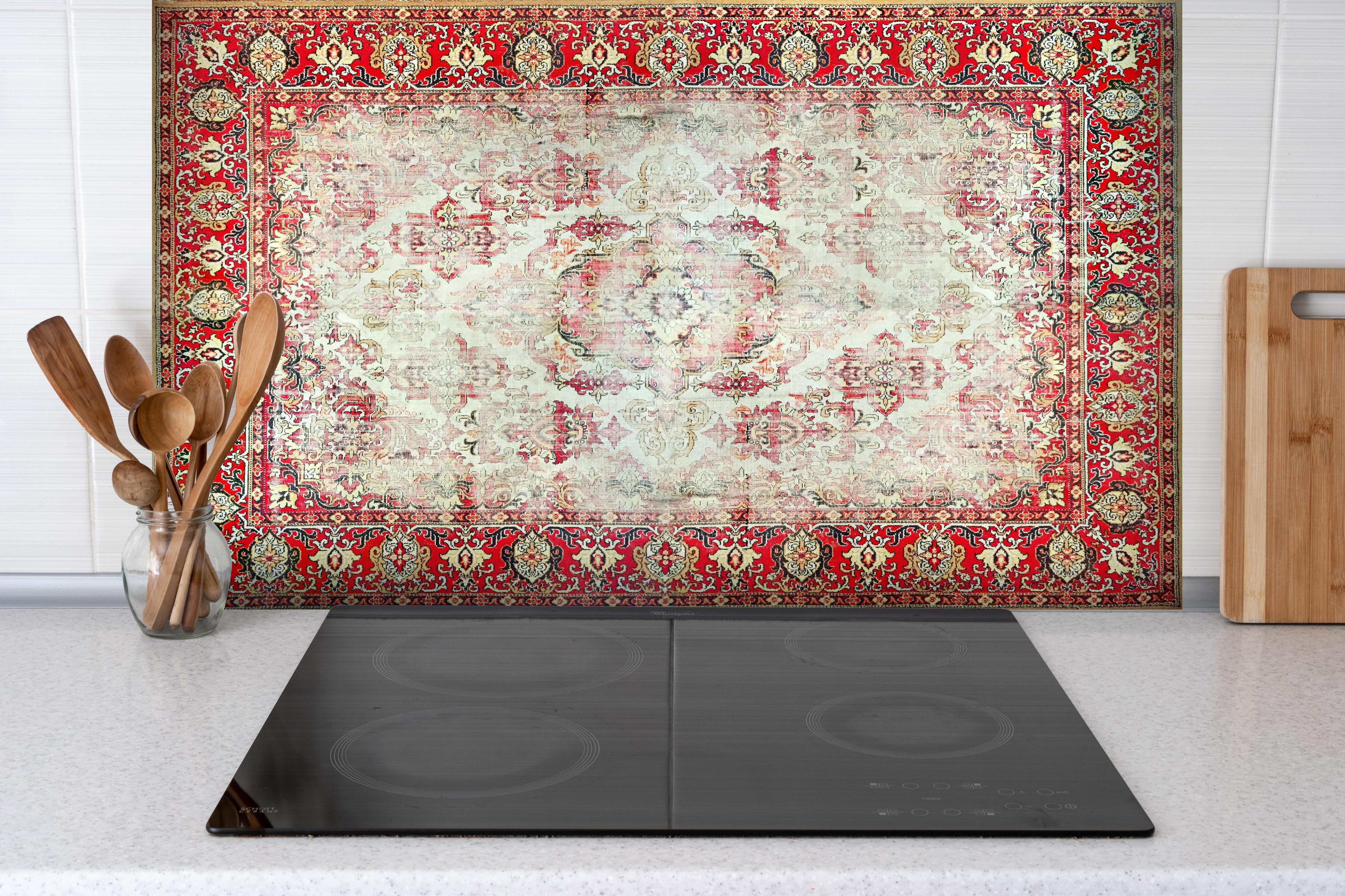 Spritzschutz - Antiker Rot-Beige-Wollteppich mit Muster hinter einem Cerankochfeld zwischen Holz-Kochutensilien
