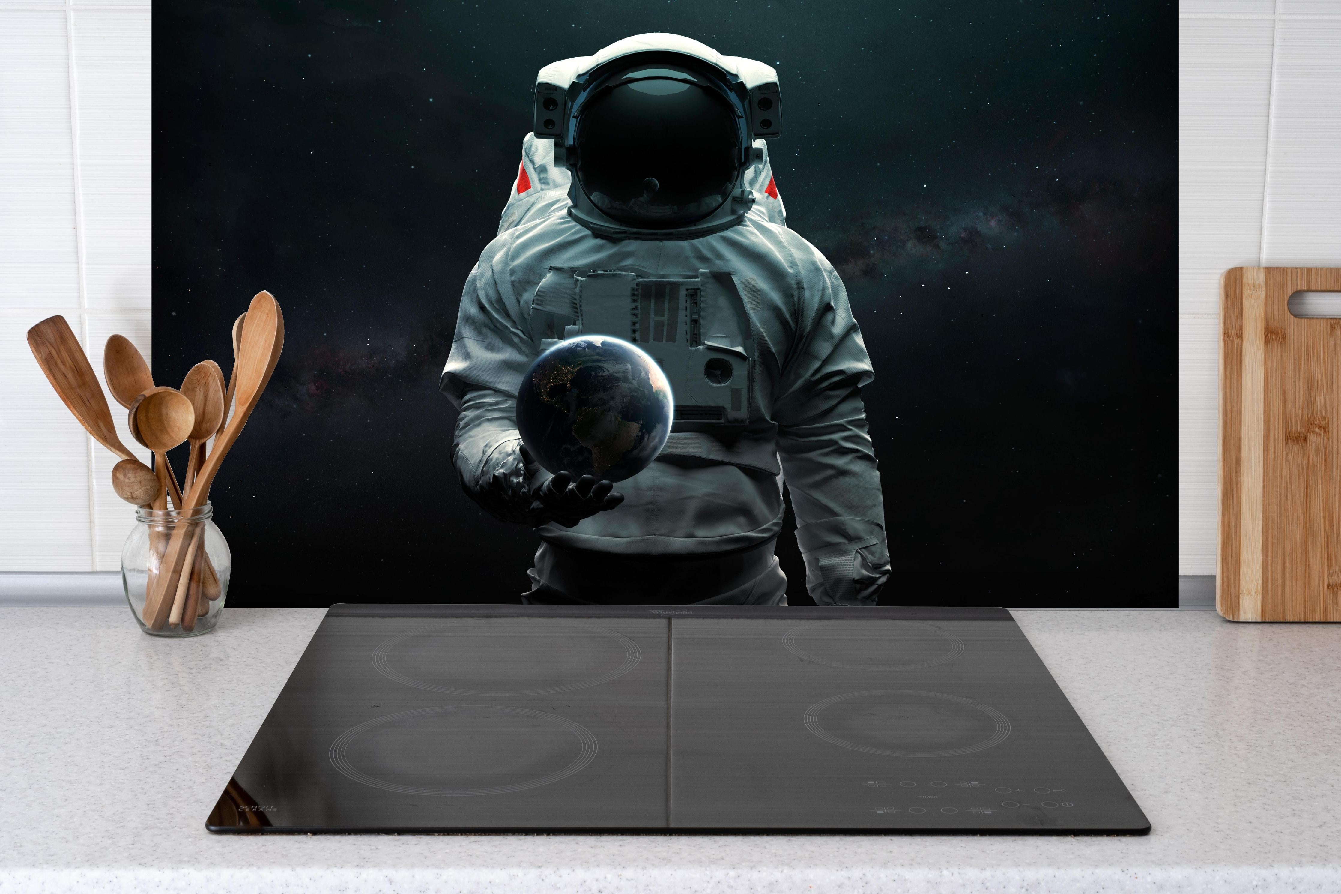 Spritzschutz - Astronaut hält Erde 3D-Kunst Sci-Fi hinter einem Cerankochfeld zwischen Holz-Kochutensilien
