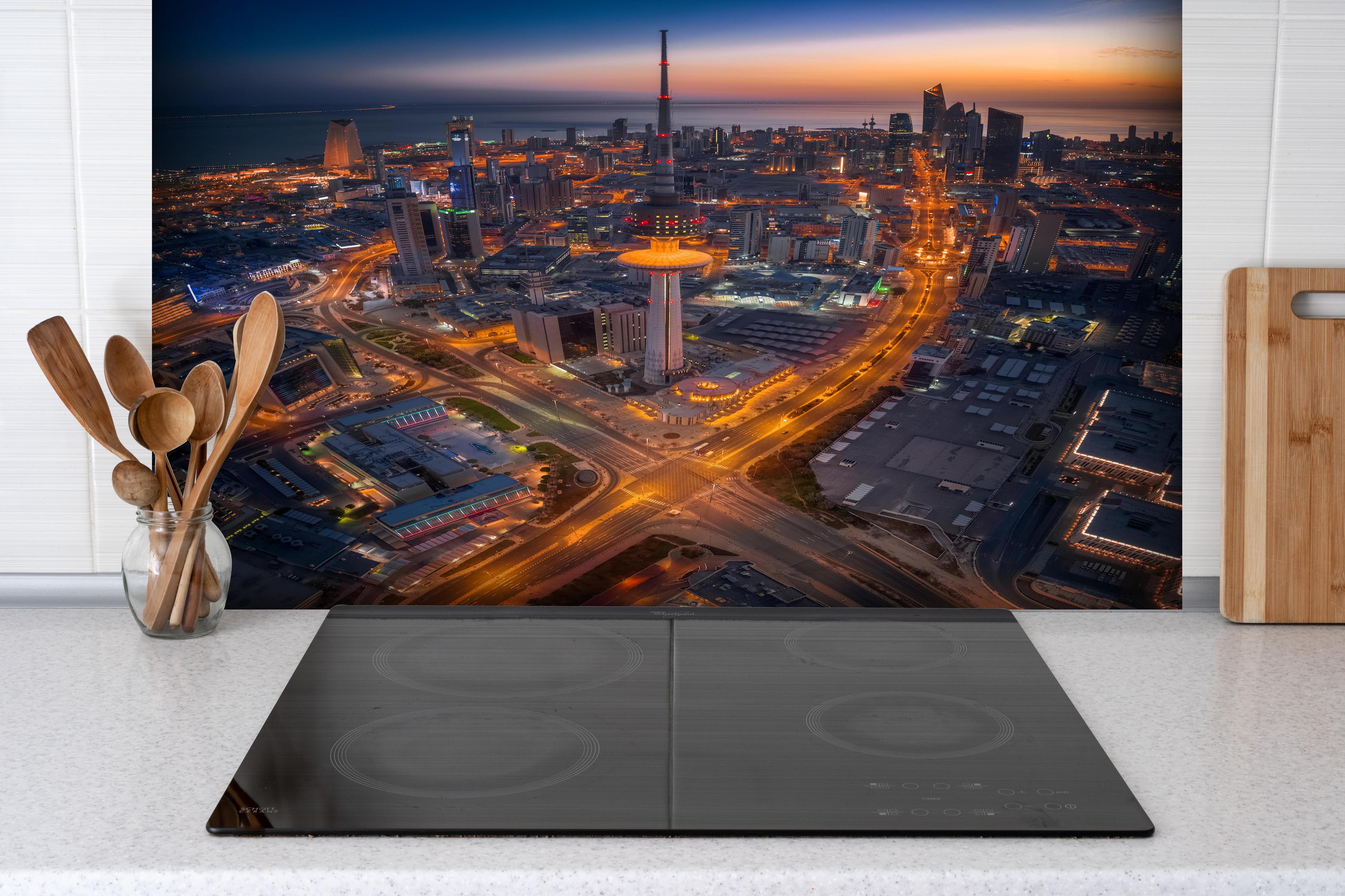 Spritzschutz - Atemberaubendes Abendpanorama Kuwait City hinter einem Cerankochfeld zwischen Holz-Kochutensilien
