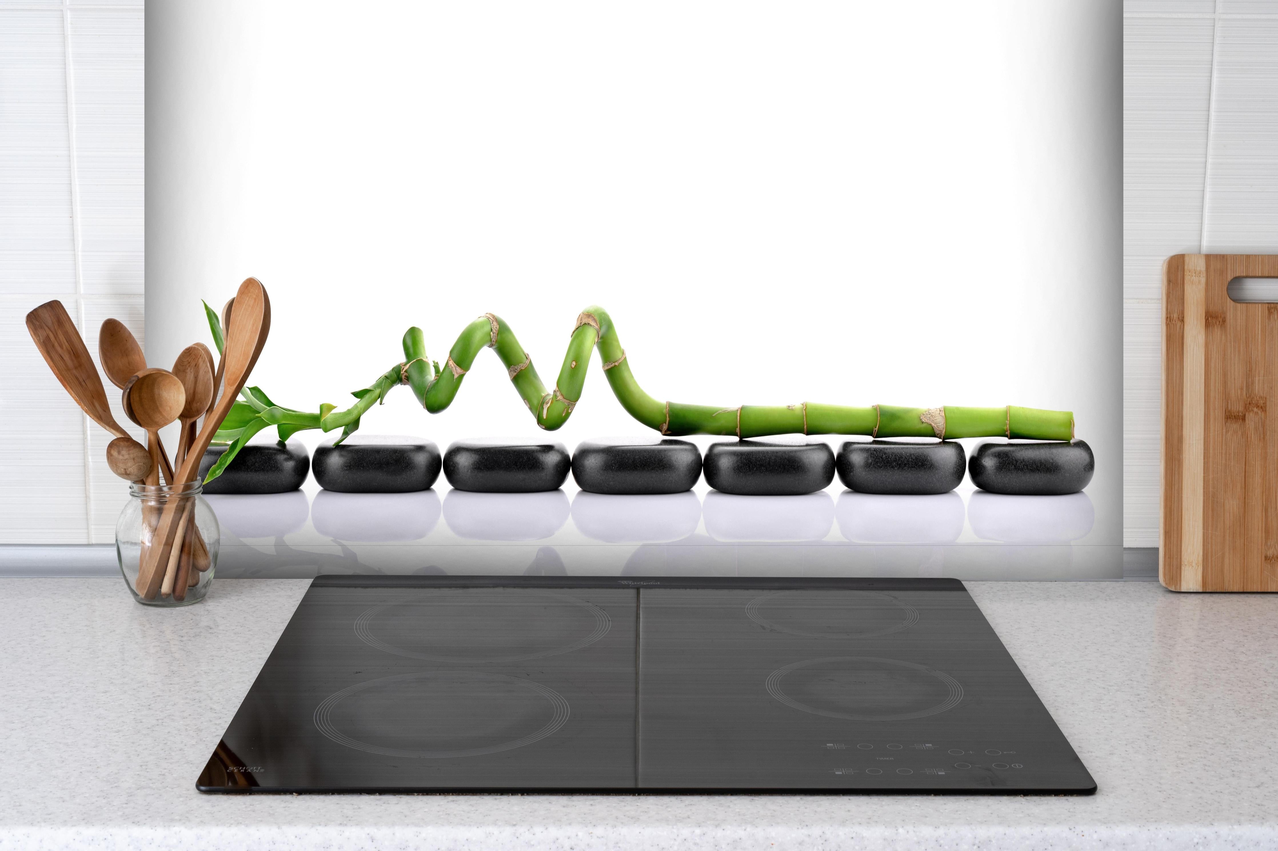 Spritzschutz - Bambusstangen auf glatten Basaltsteinen hinter einem Cerankochfeld zwischen Holz-Kochutensilien
