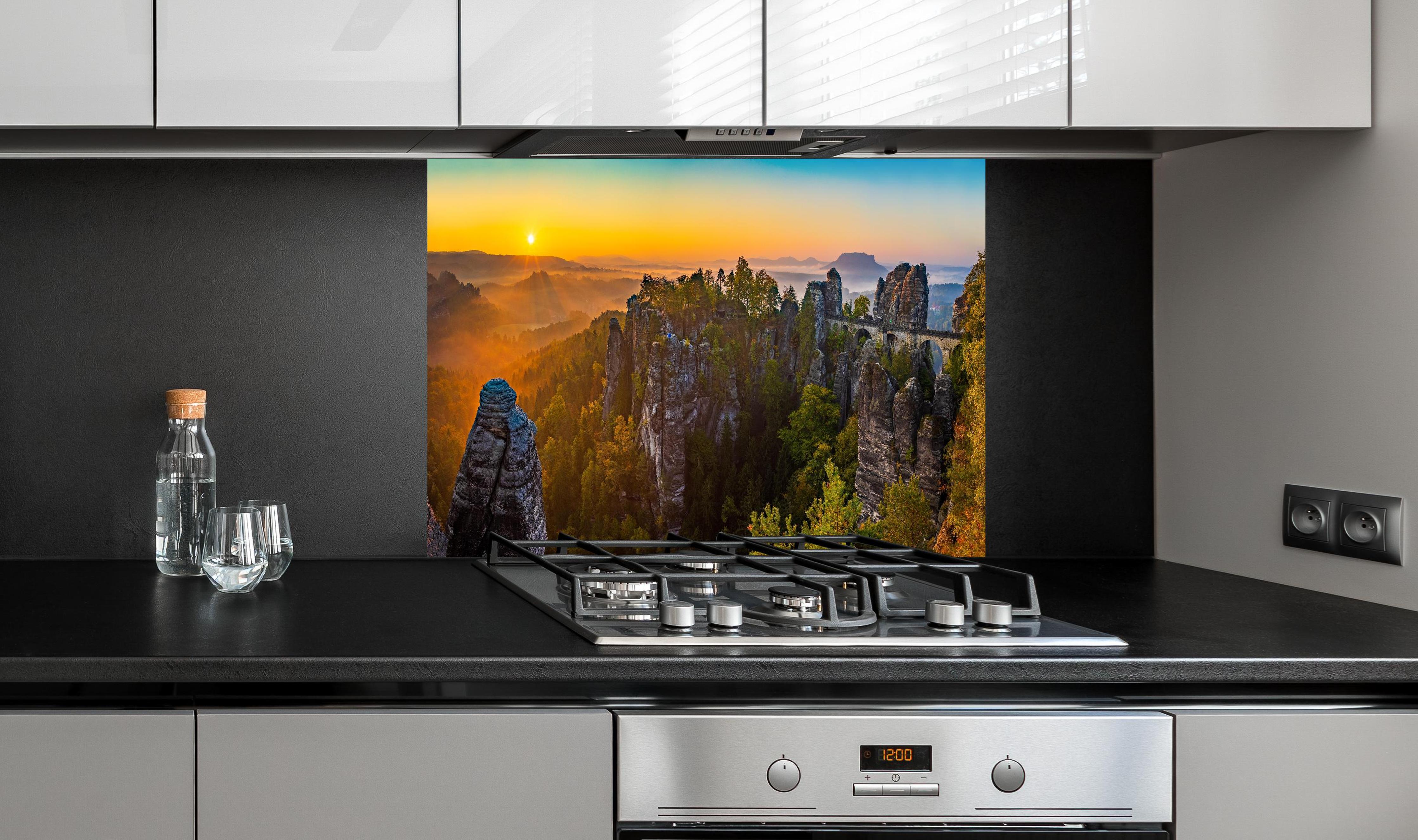 Spritzschutz - Basteibrücke Sonnenaufgang Felsformationen hinter einem Cerankochfeld zwischen Holz-Kochutensilien
