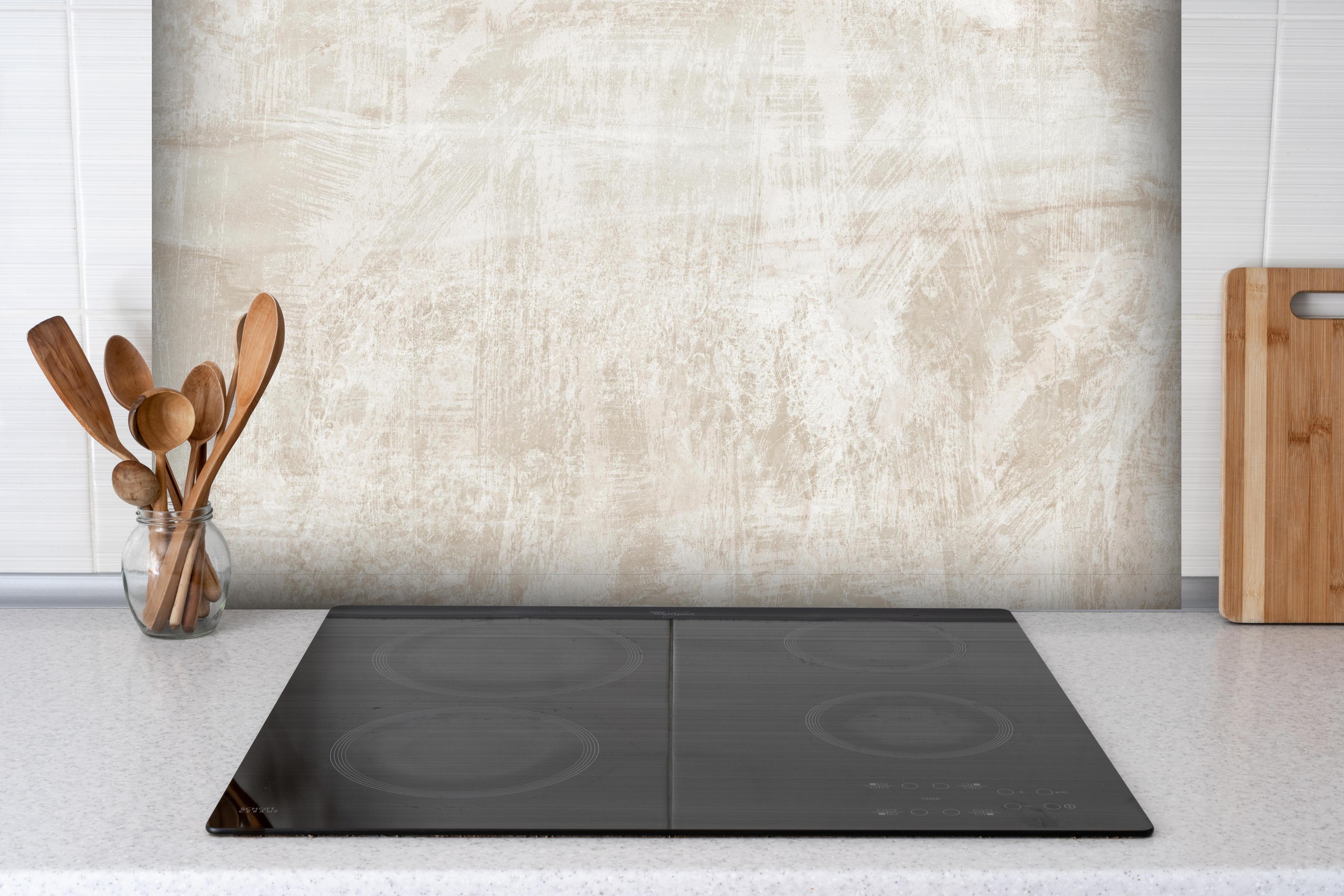 Spritzschutz - Beigefarbener Hintergrund hinter einem Cerankochfeld zwischen Holz-Kochutensilien
