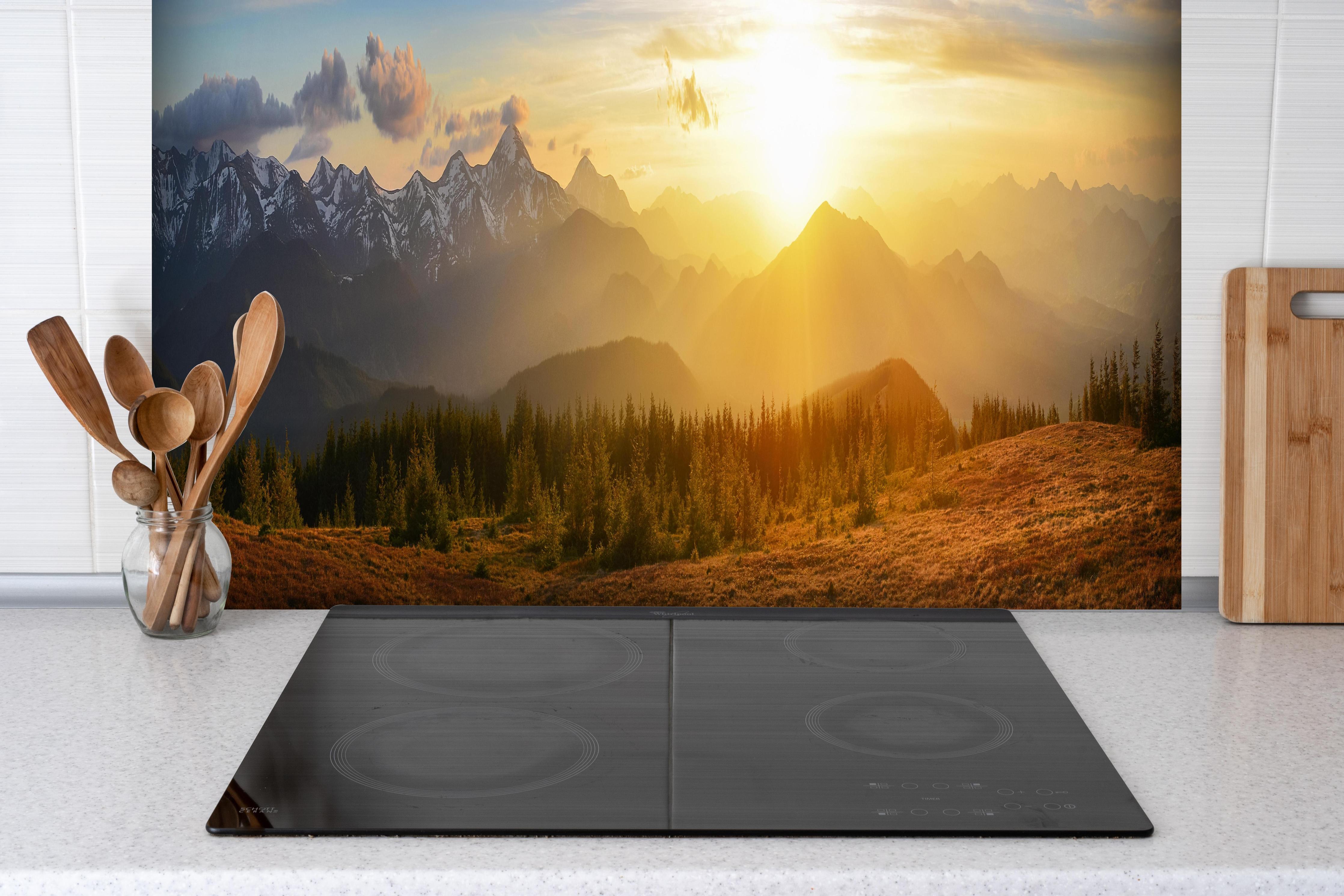 Spritzschutz - Berge im Sonnenuntergang hinter einem Cerankochfeld zwischen Holz-Kochutensilien
