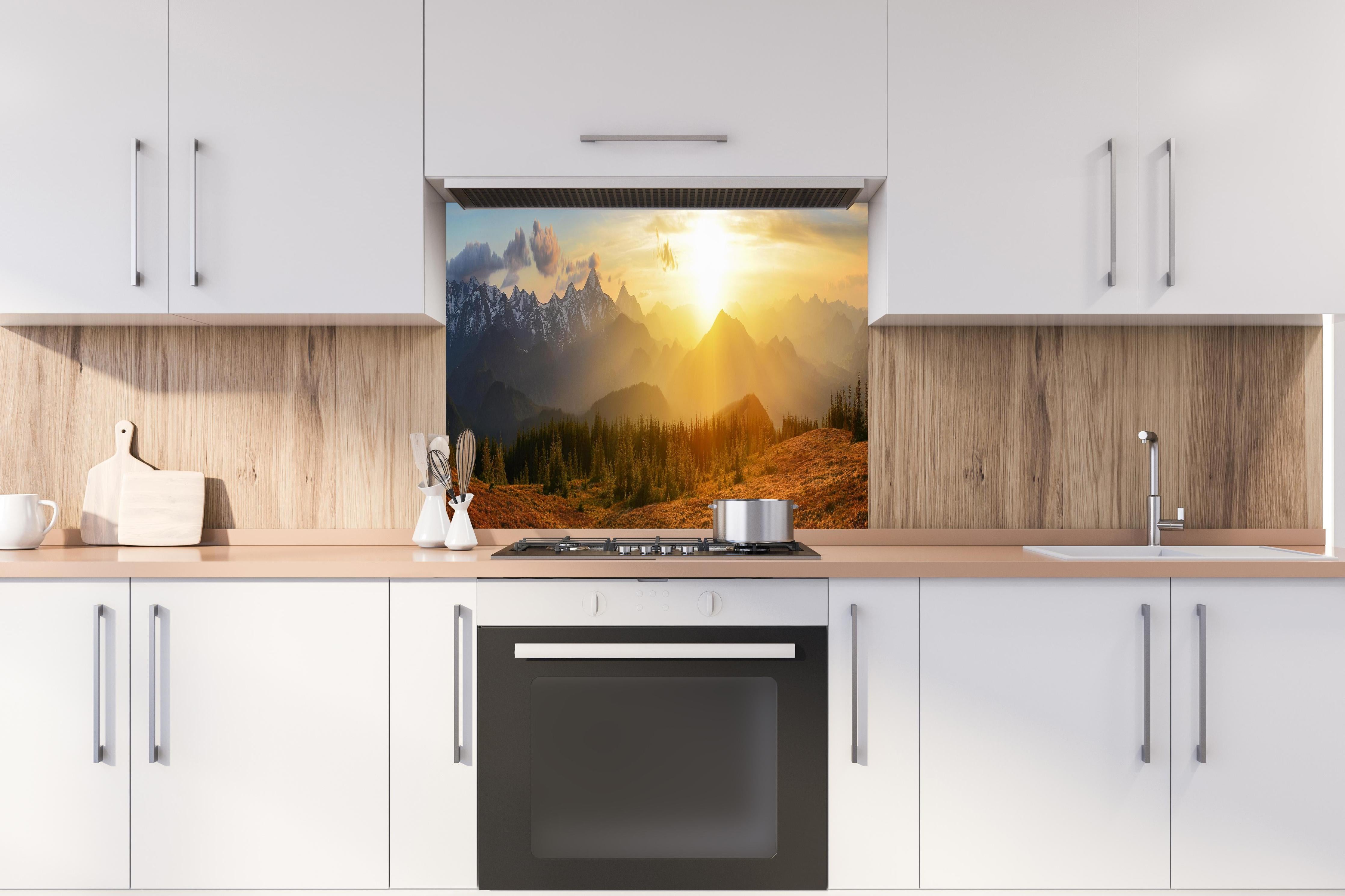 Spritzschutz - Berge im Sonnenuntergang hinter einem Cerankochfeld zwischen Holz-Kochutensilien
