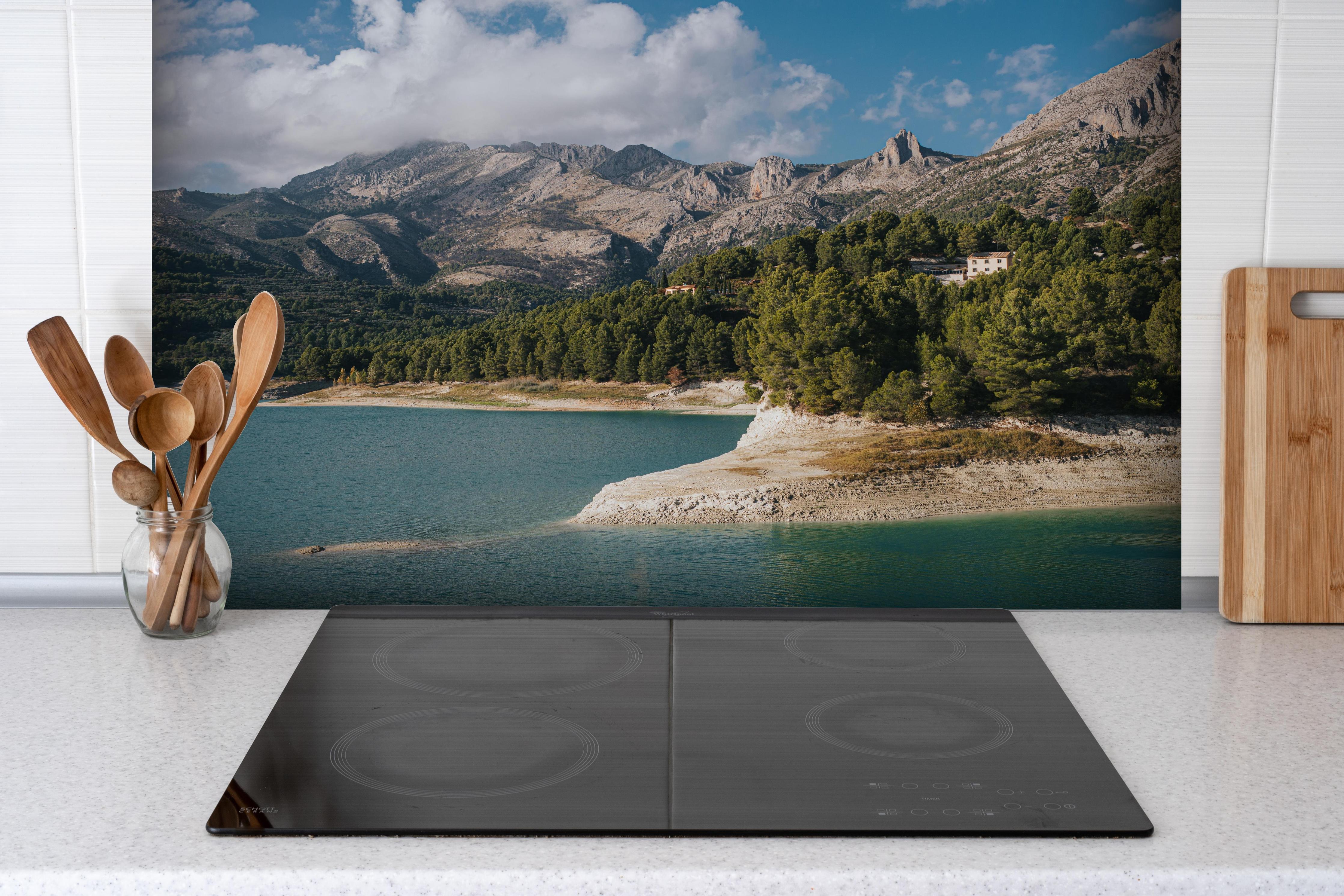 Spritzschutz - Bergsee mit Wäldern und Berge hinter einem Cerankochfeld zwischen Holz-Kochutensilien

