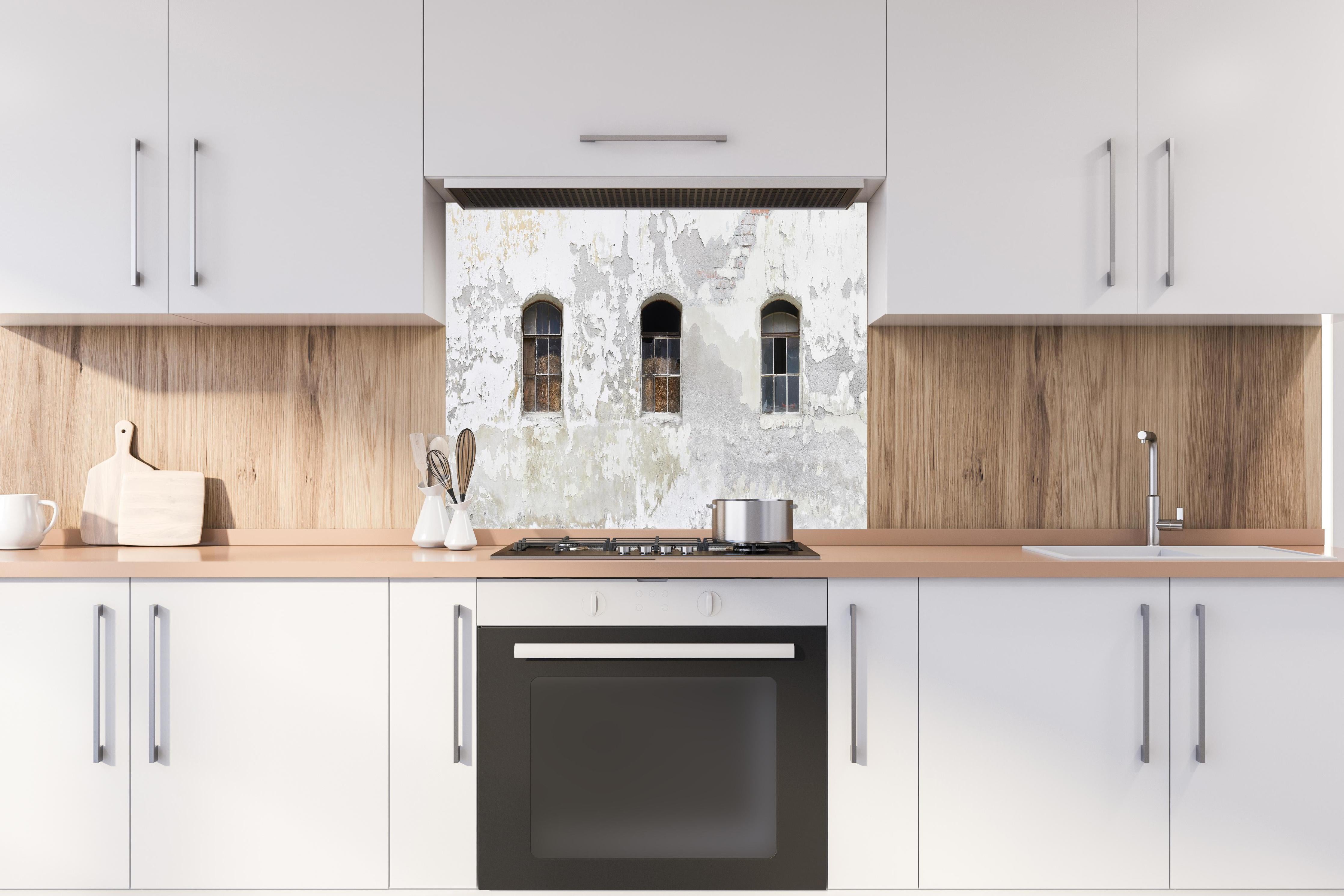 Spritzschutz - Beschädigte Fenster einer veralteten Hauswand hinter einem Cerankochfeld zwischen Holz-Kochutensilien
