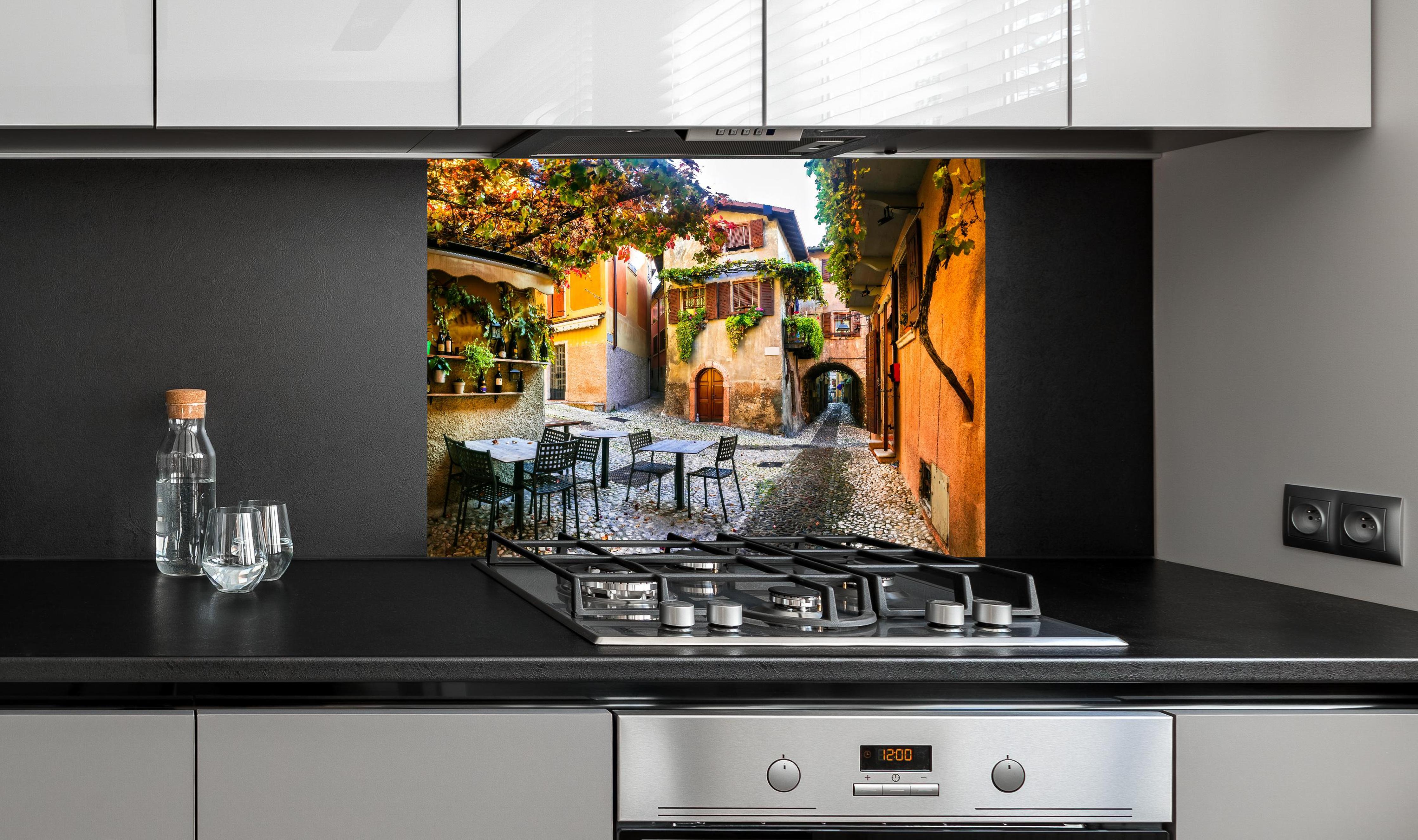 Spritzschutz - Bezaubernde alte Gasse in Malcesine hinter einem Cerankochfeld zwischen Holz-Kochutensilien
