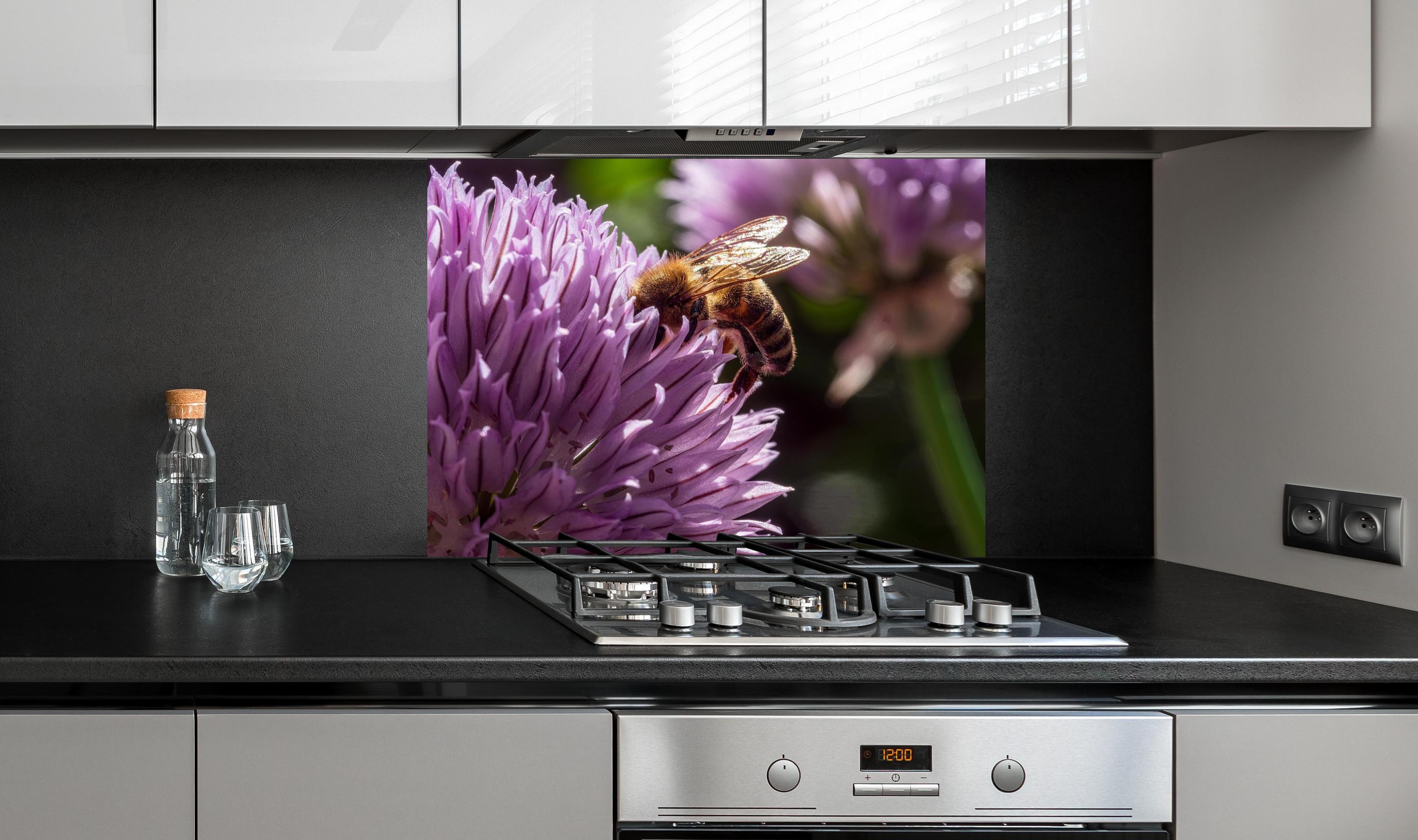 Spritzschutz - Biene auf lila Blüte Makroaufnahme hinter einem Cerankochfeld zwischen Holz-Kochutensilien
