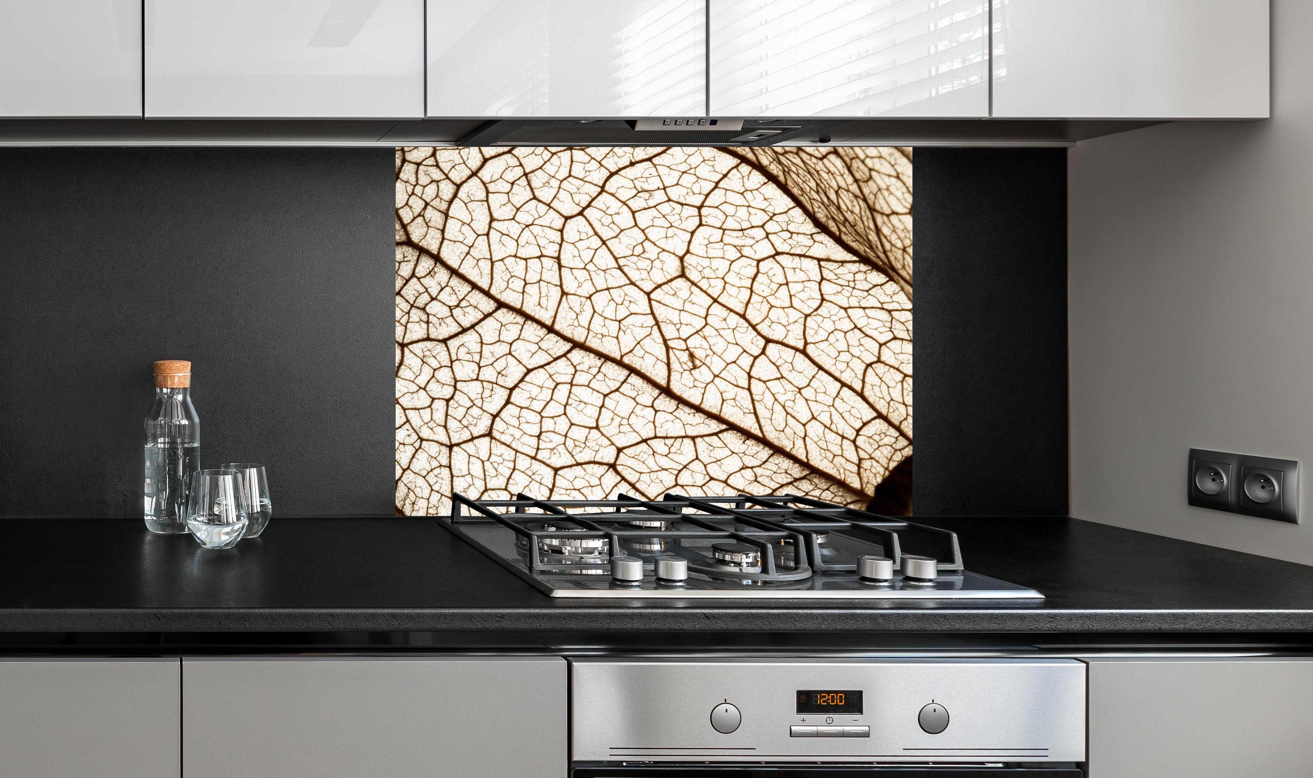 Spritzschutz - Blatttextur im Detail hinter einem Cerankochfeld zwischen Holz-Kochutensilien
