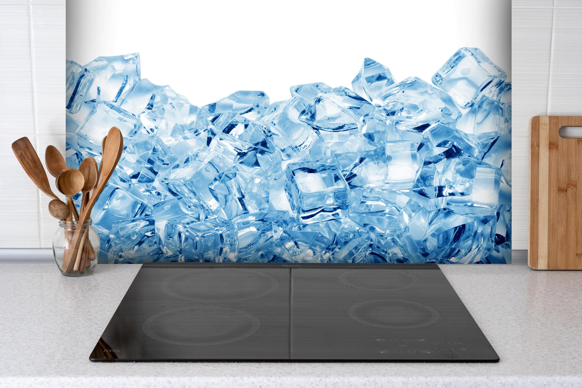 Spritzschutz - Blau kristallklarer Eiswürfel hinter einem Cerankochfeld zwischen Holz-Kochutensilien
