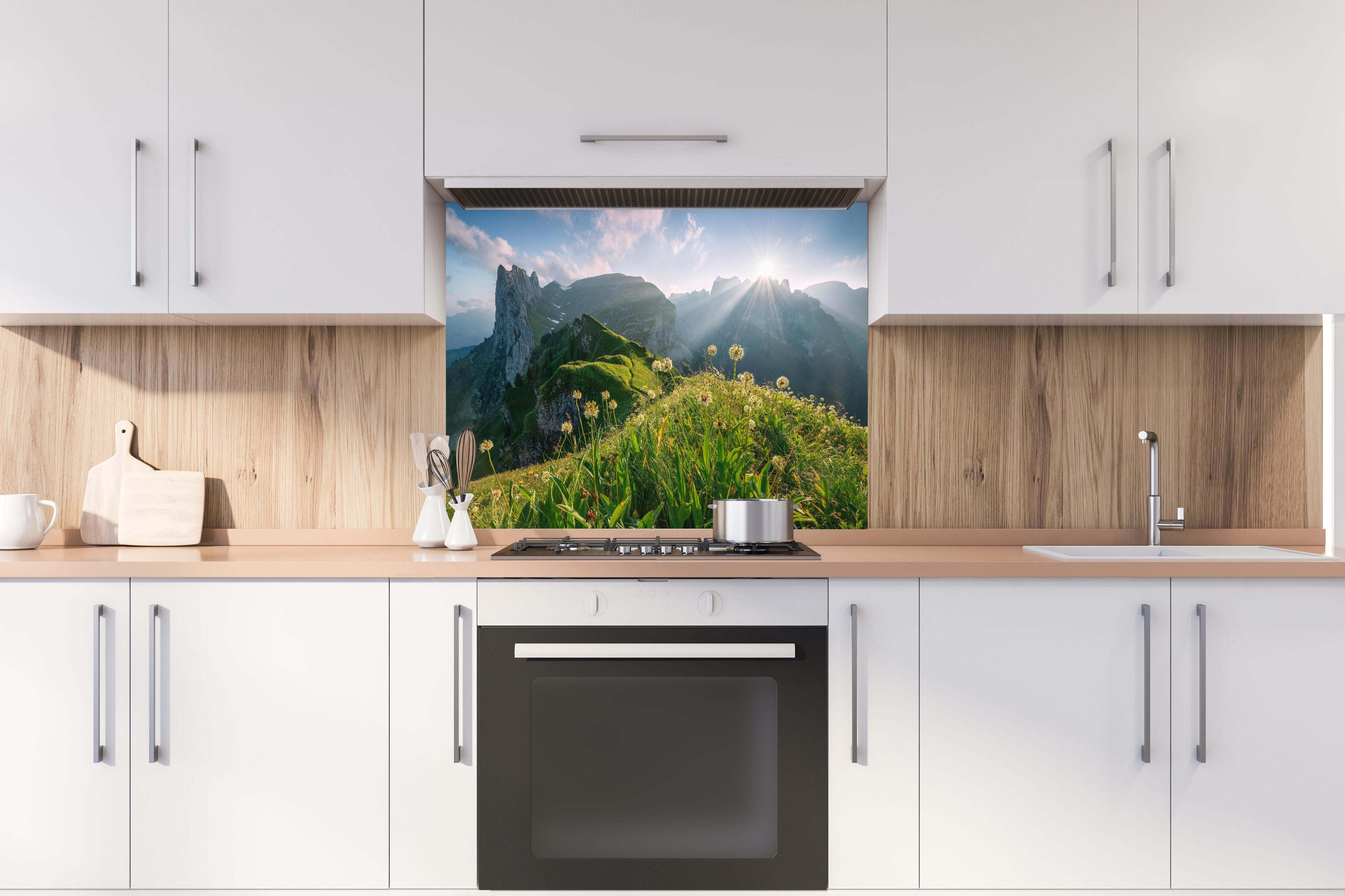 Spritzschutz - Blühende Alpenwiesen bei Sonnenaufgang hinter einem Cerankochfeld zwischen Holz-Kochutensilien
