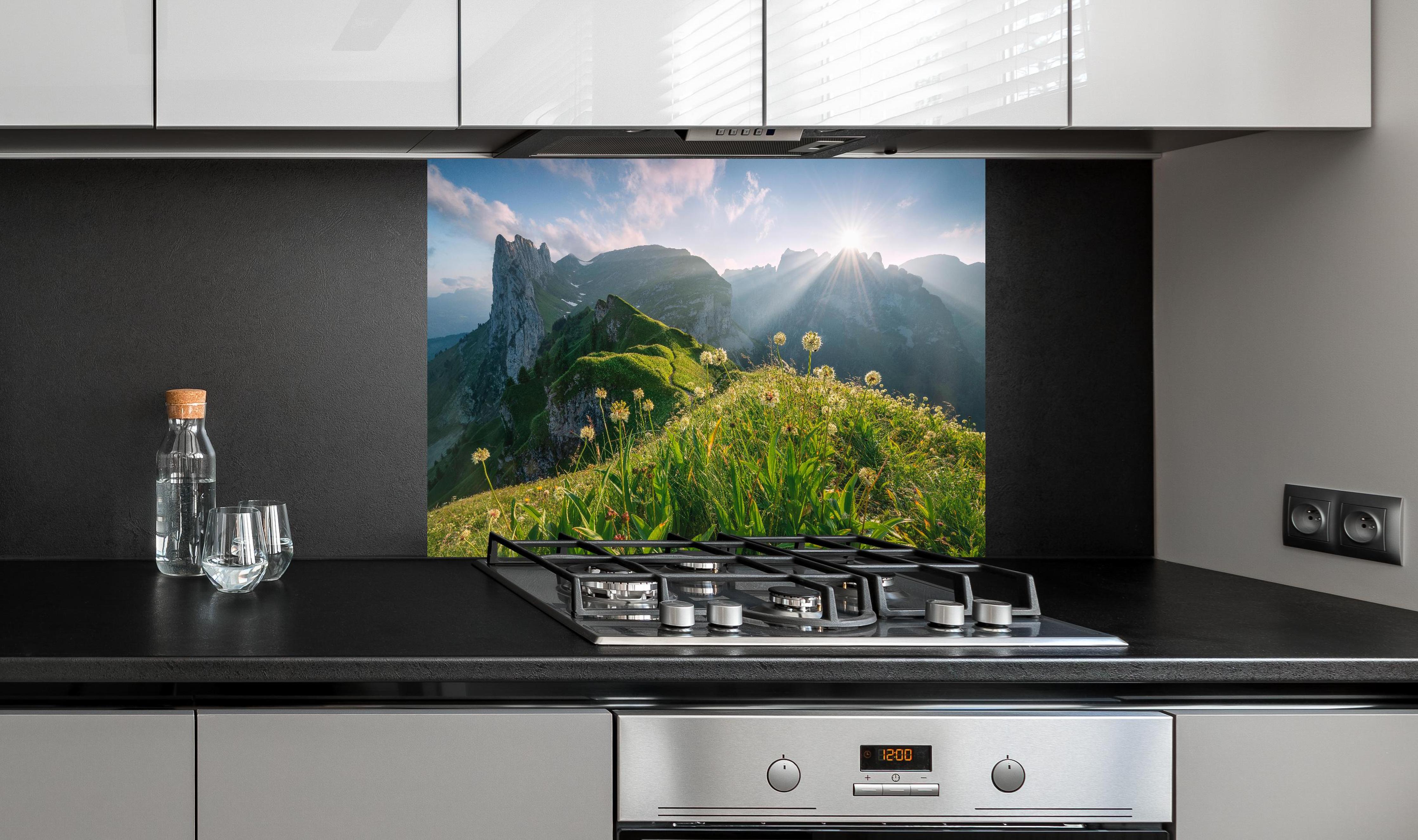 Spritzschutz - Blühende Alpenwiesen bei Sonnenaufgang hinter einem Cerankochfeld zwischen Holz-Kochutensilien
