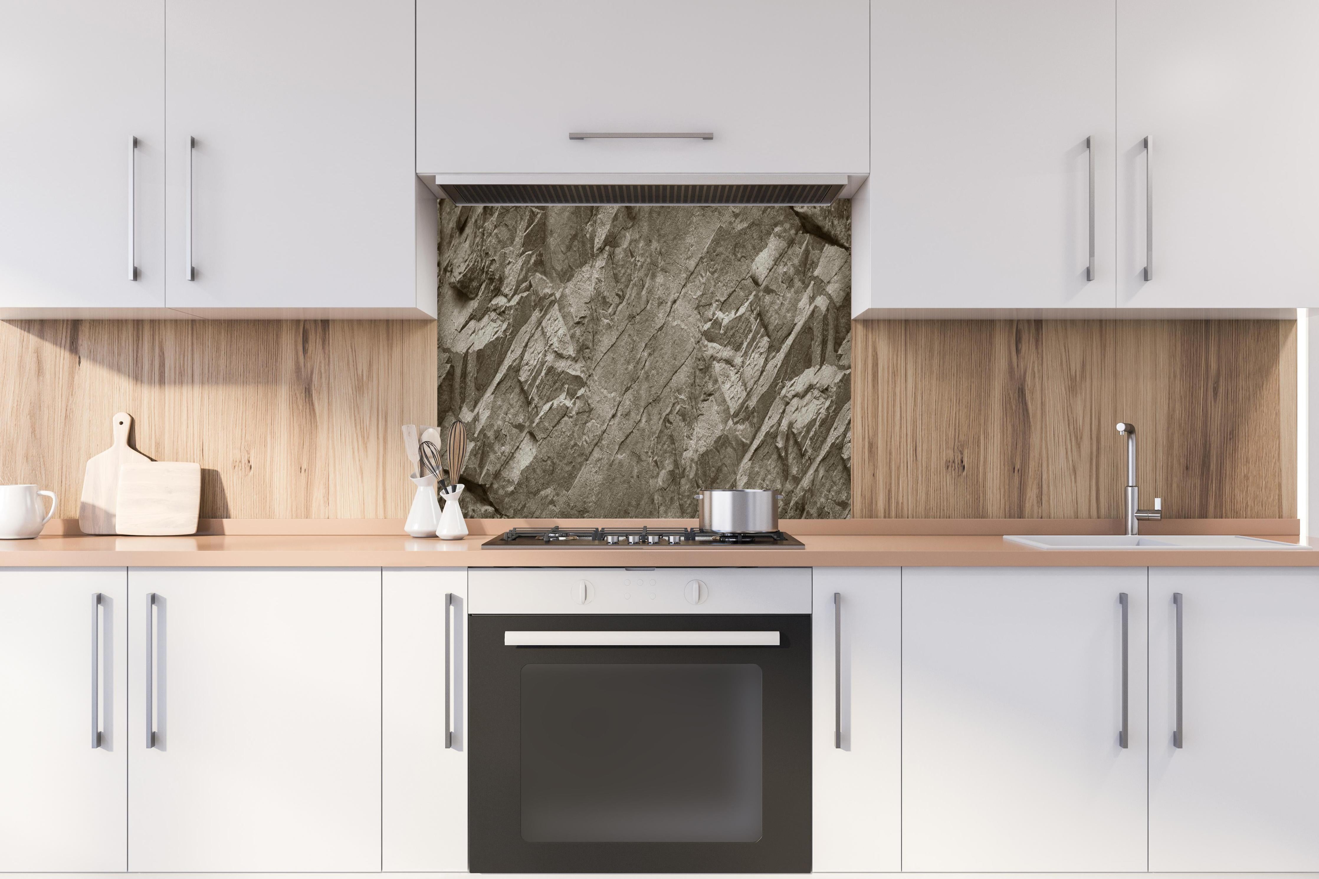 Spritzschutz - Breite braun-graue Felsstruktur hinter einem Cerankochfeld zwischen Holz-Kochutensilien
