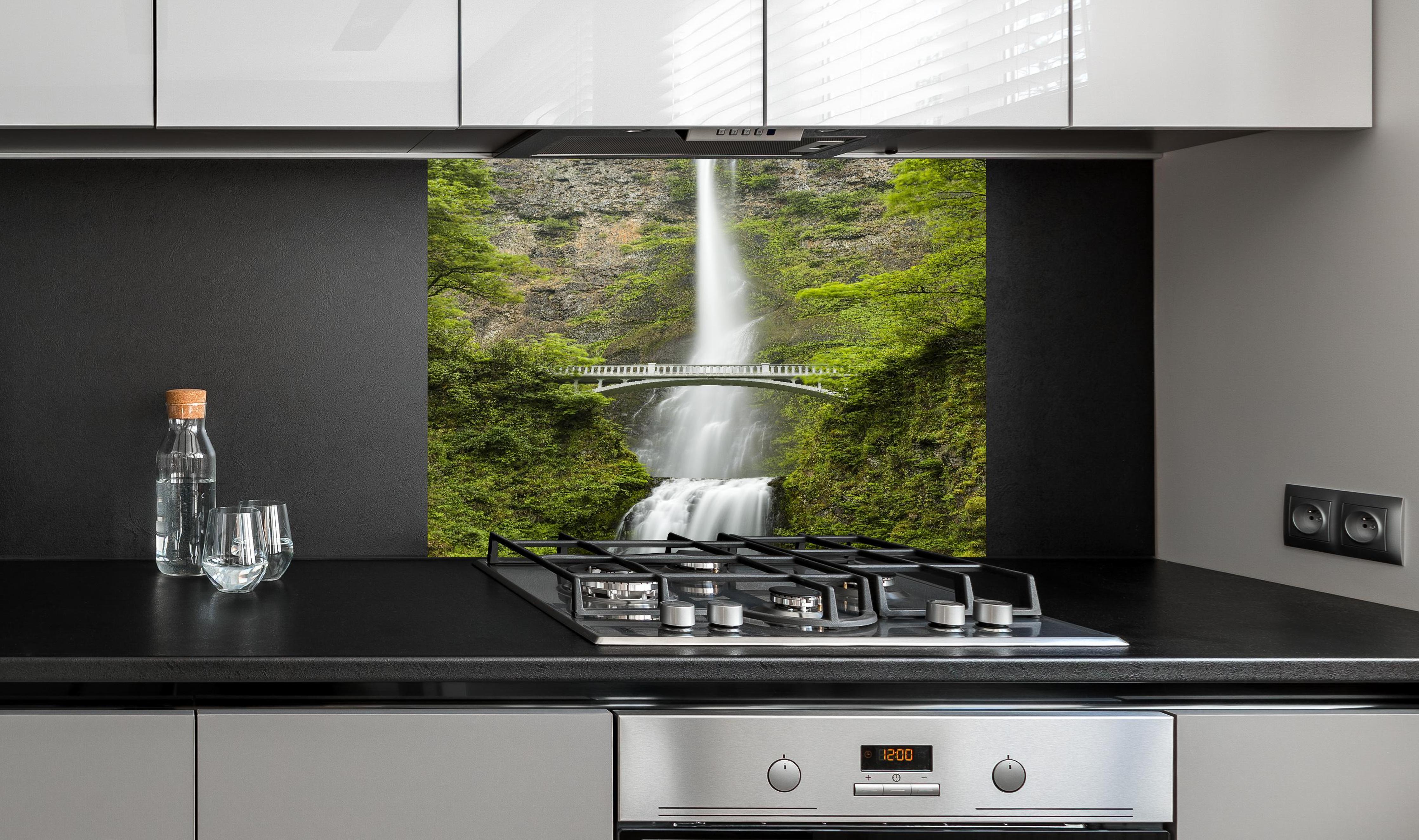 Spritzschutz - Brücke vor grünem Wasserfall Natur hinter einem Cerankochfeld zwischen Holz-Kochutensilien
