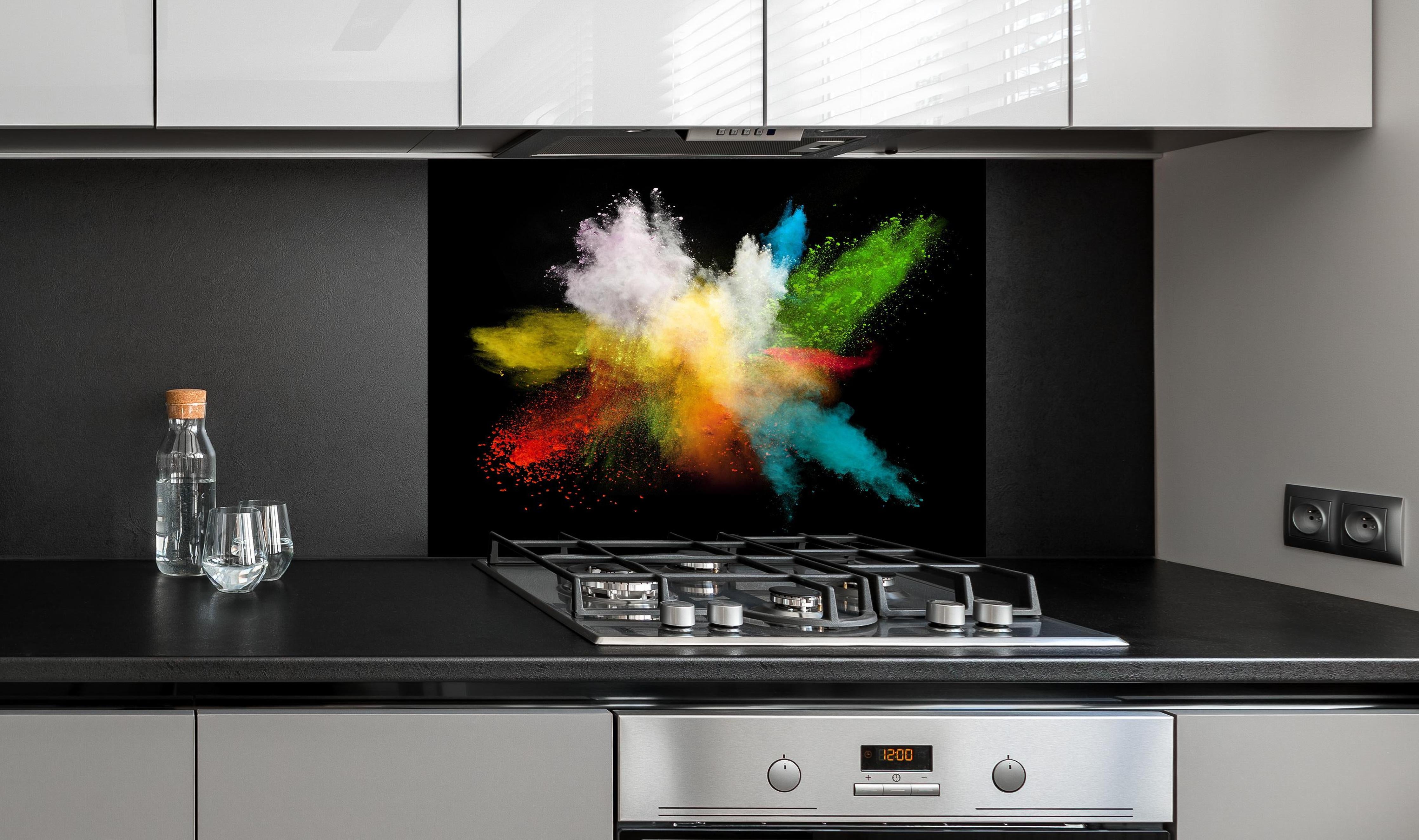 Spritzschutz - Bunte Farbexplosion auf schwarzem Hintergrund hinter einem Cerankochfeld zwischen Holz-Kochutensilien
