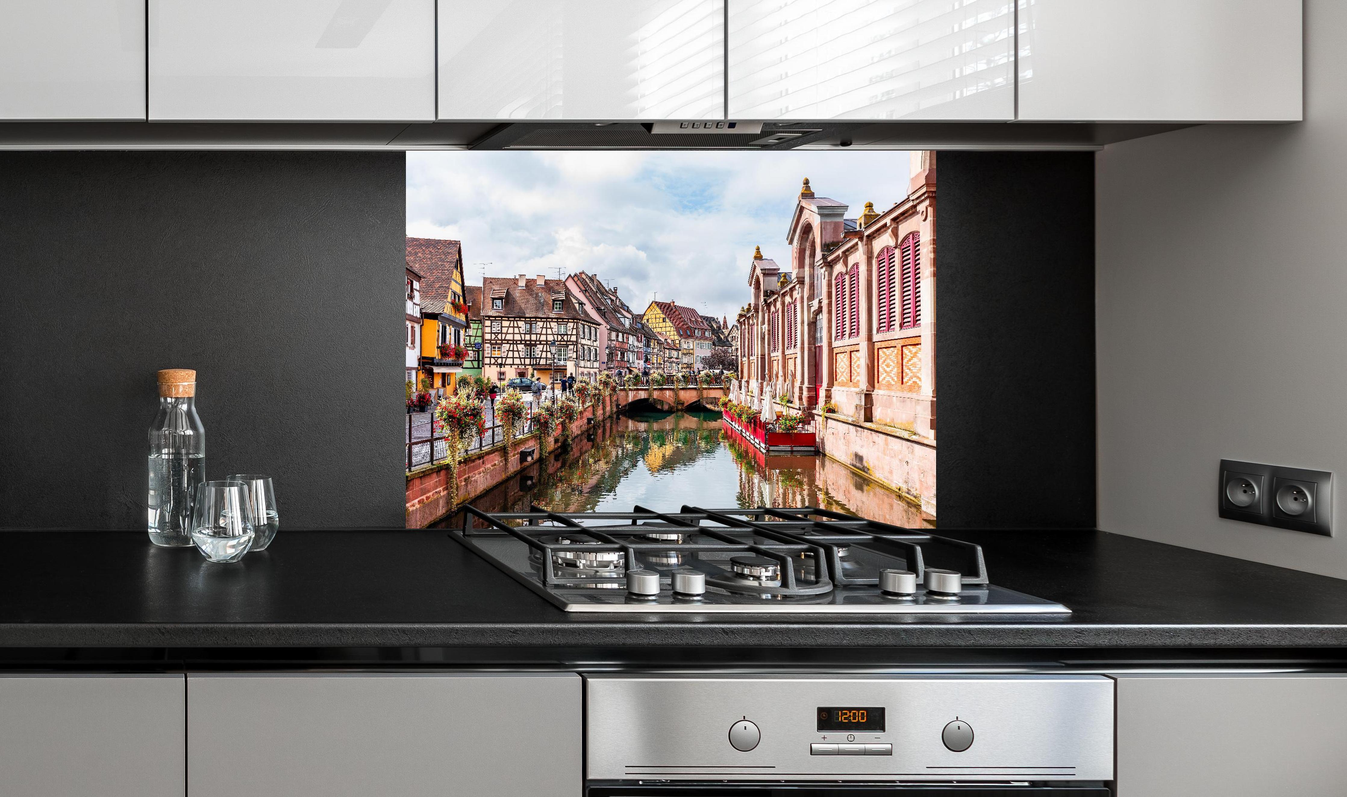 Spritzschutz - Bunte Häuser am Fluss in Colmar hinter einem Cerankochfeld zwischen Holz-Kochutensilien
