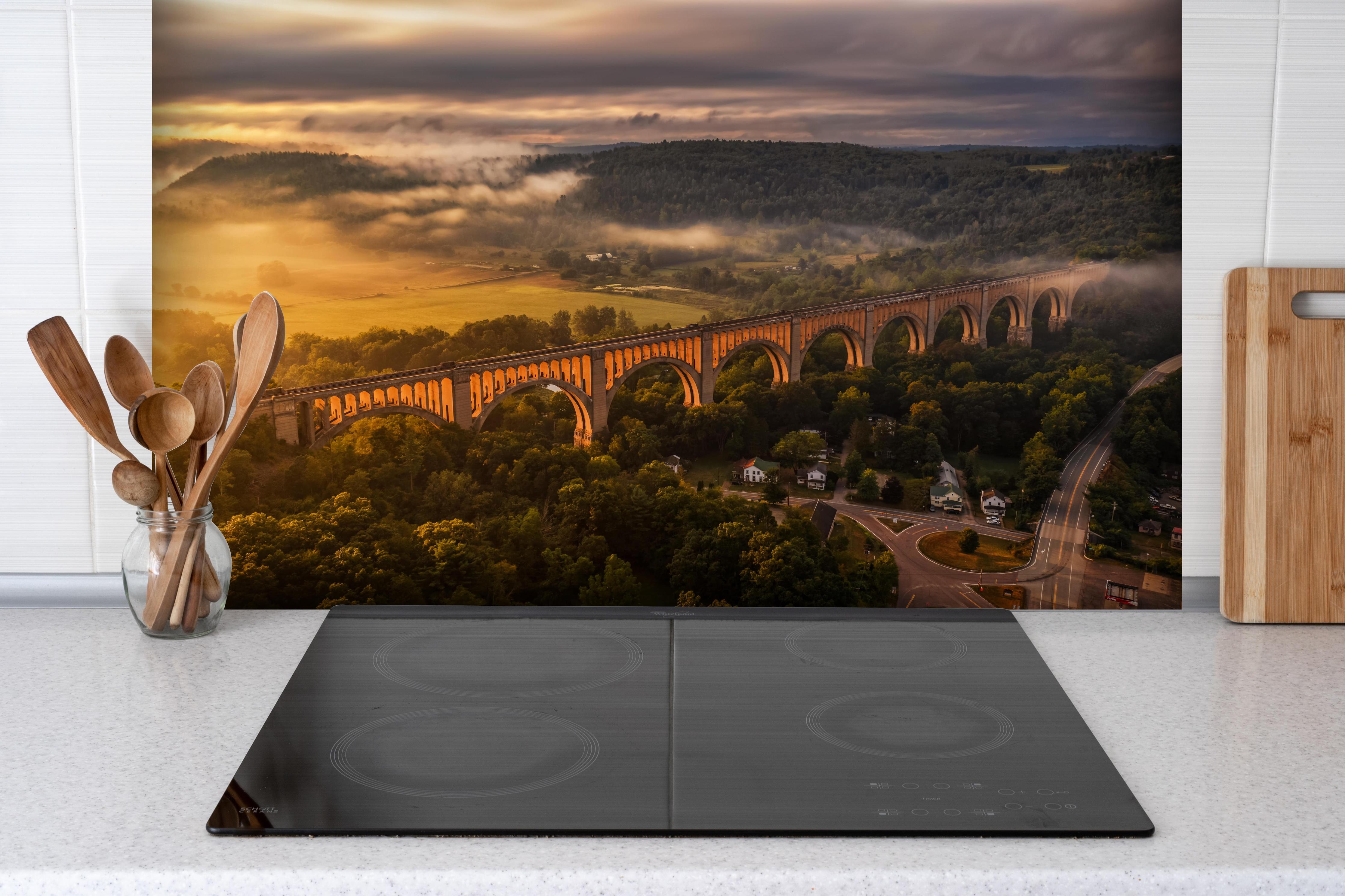 Spritzschutz - Buntes Dorf Mediterranes Flair hinter einem Cerankochfeld zwischen Holz-Kochutensilien
