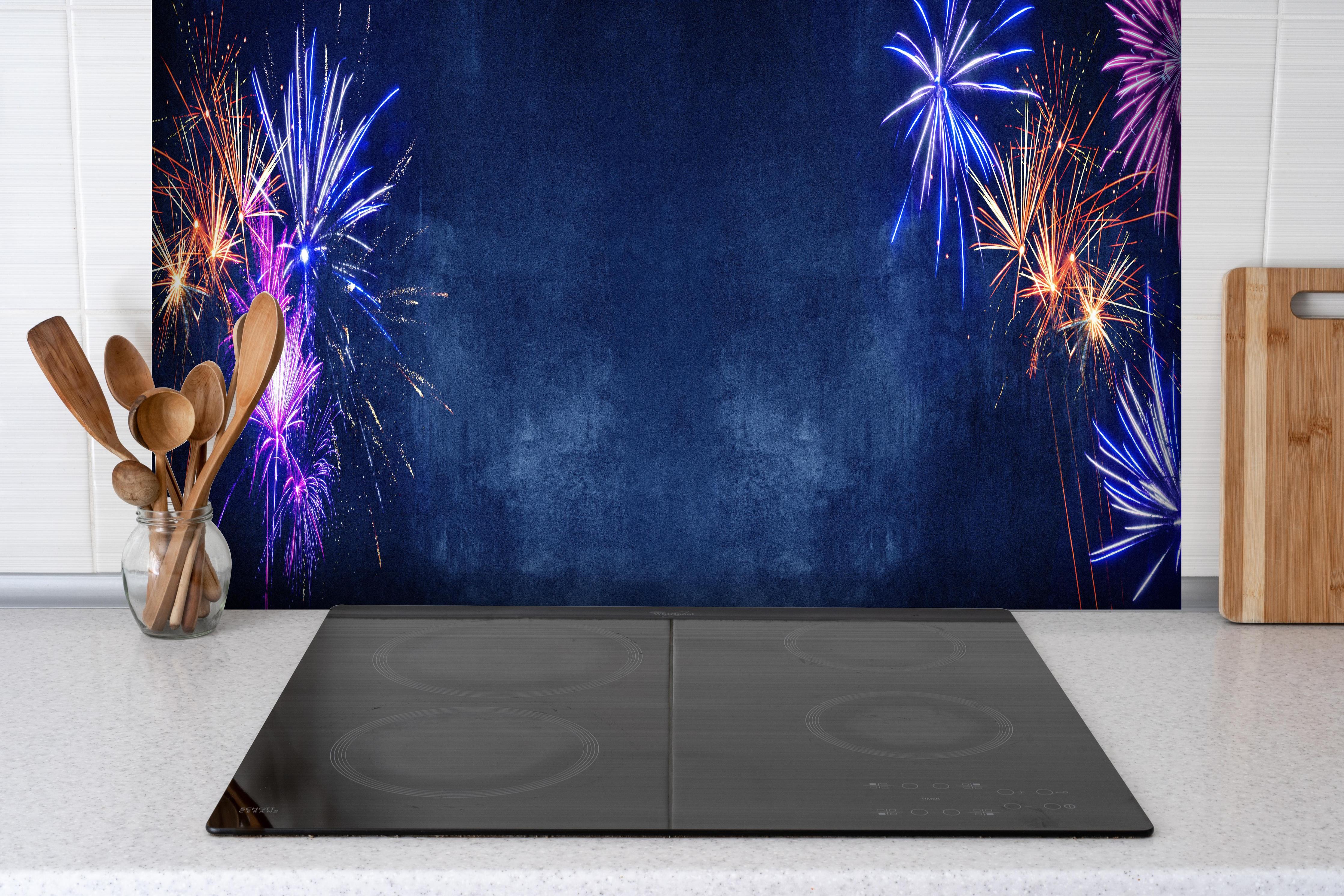Spritzschutz - Buntes Silvester-Feuerwerk am Dunkelblauen Himmel hinter einem Cerankochfeld zwischen Holz-Kochutensilien
