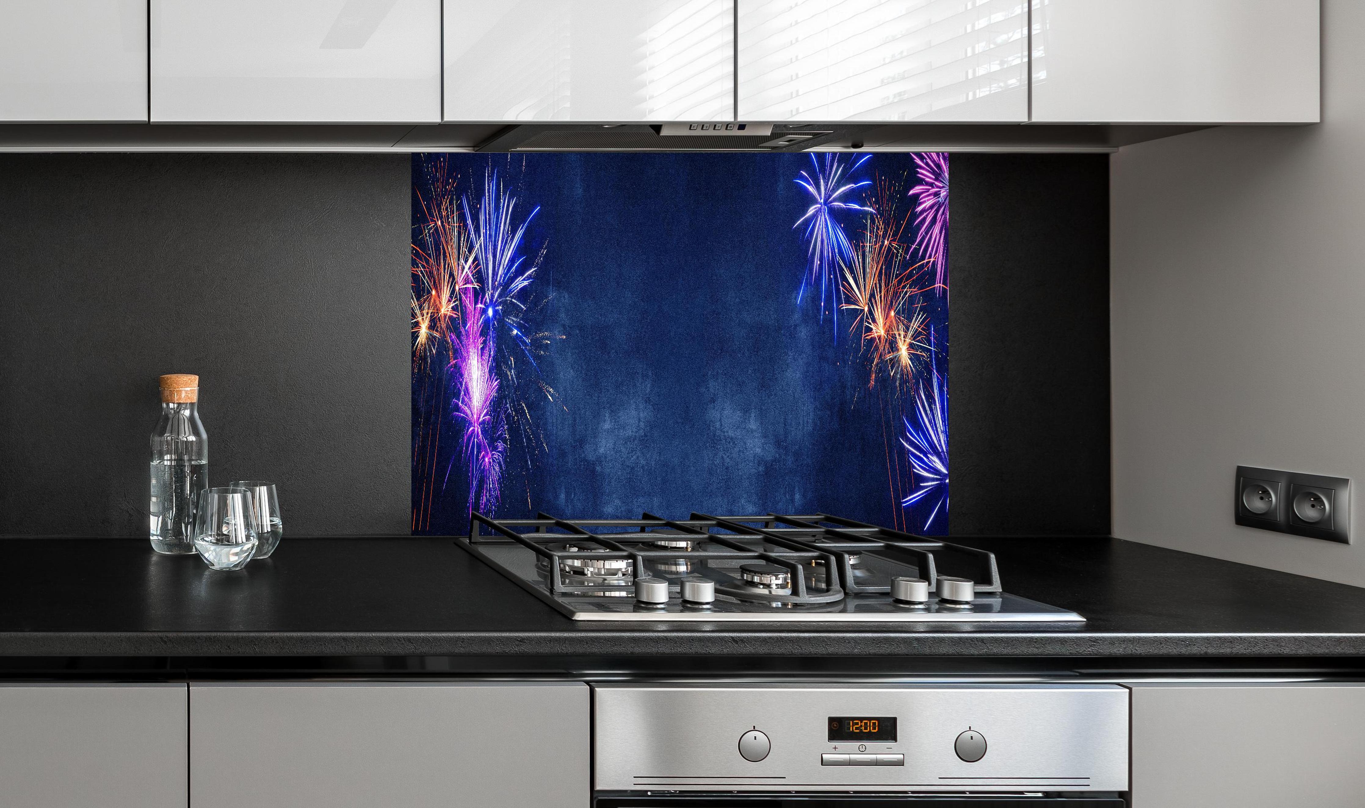 Spritzschutz - Buntes Silvester-Feuerwerk am Dunkelblauen Himmel hinter einem Cerankochfeld zwischen Holz-Kochutensilien
