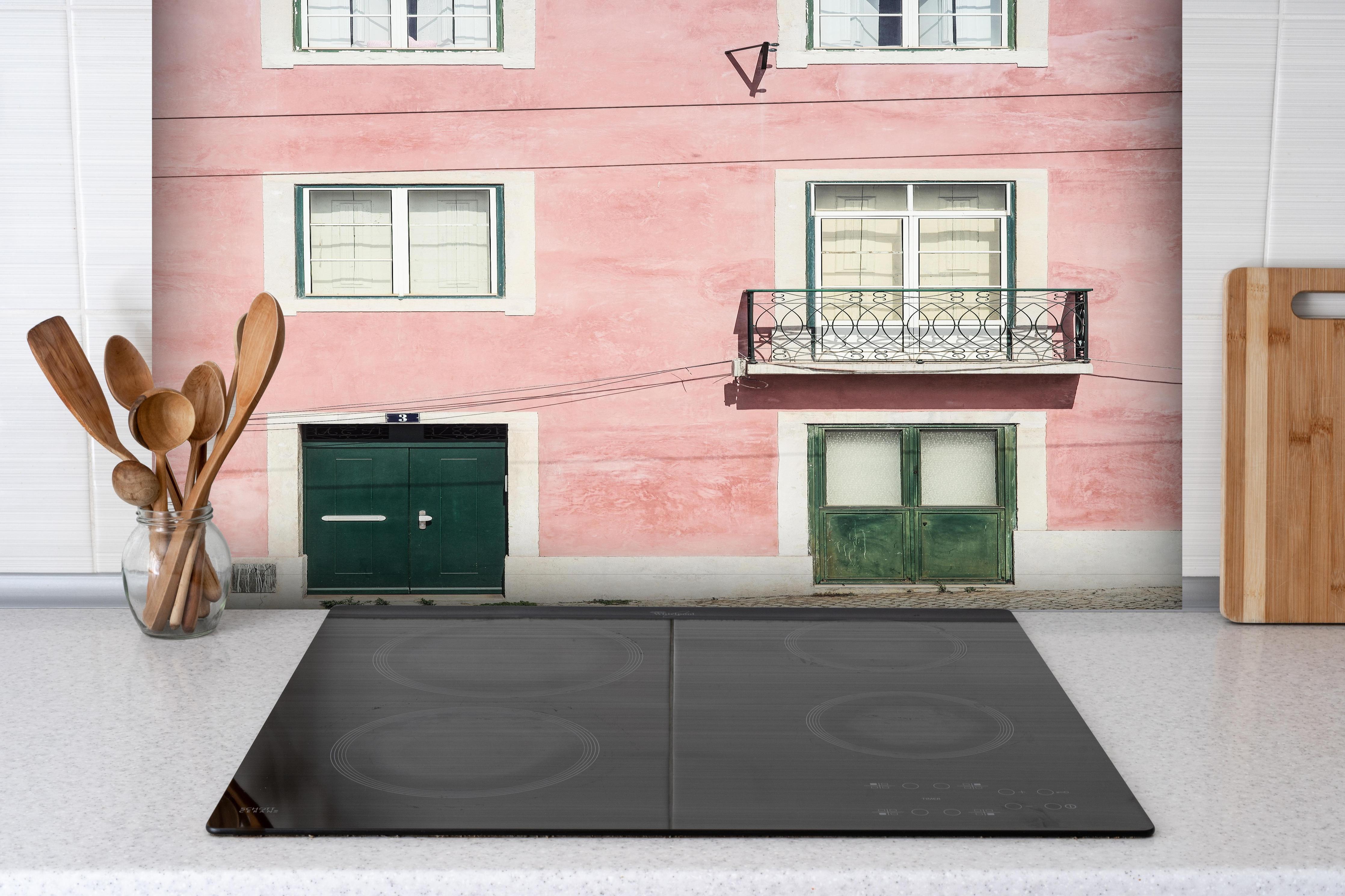 Spritzschutz - Charmante Pastellrosa Fassade mit Balkon hinter einem Cerankochfeld zwischen Holz-Kochutensilien
