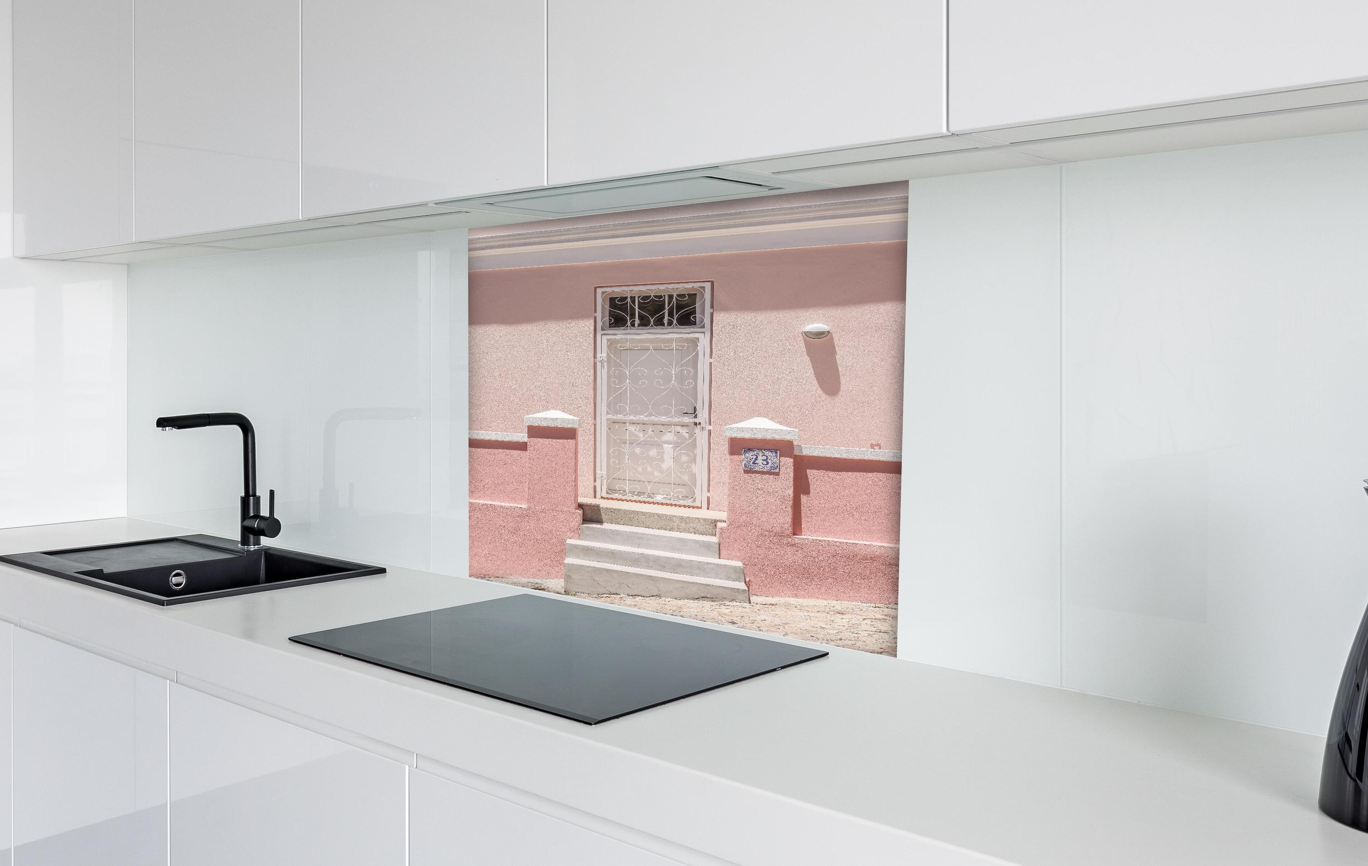 Spritzschutz - Charmante pastellrosa Hausfassade hinter einem Cerankochfeld zwischen Holz-Kochutensilien
