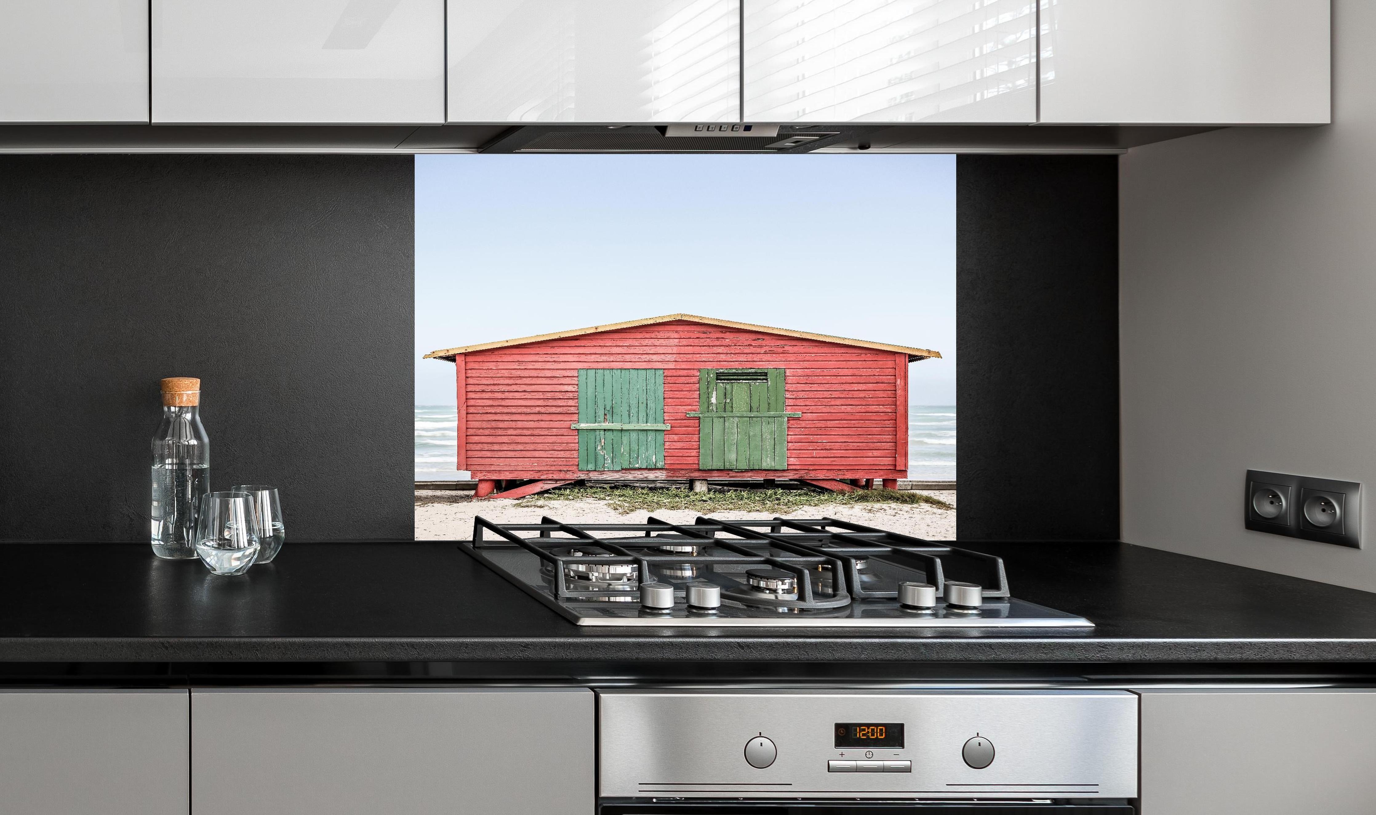 Spritzschutz - Charmante rote Strandhütte Küstenblick hinter einem Cerankochfeld zwischen Holz-Kochutensilien
