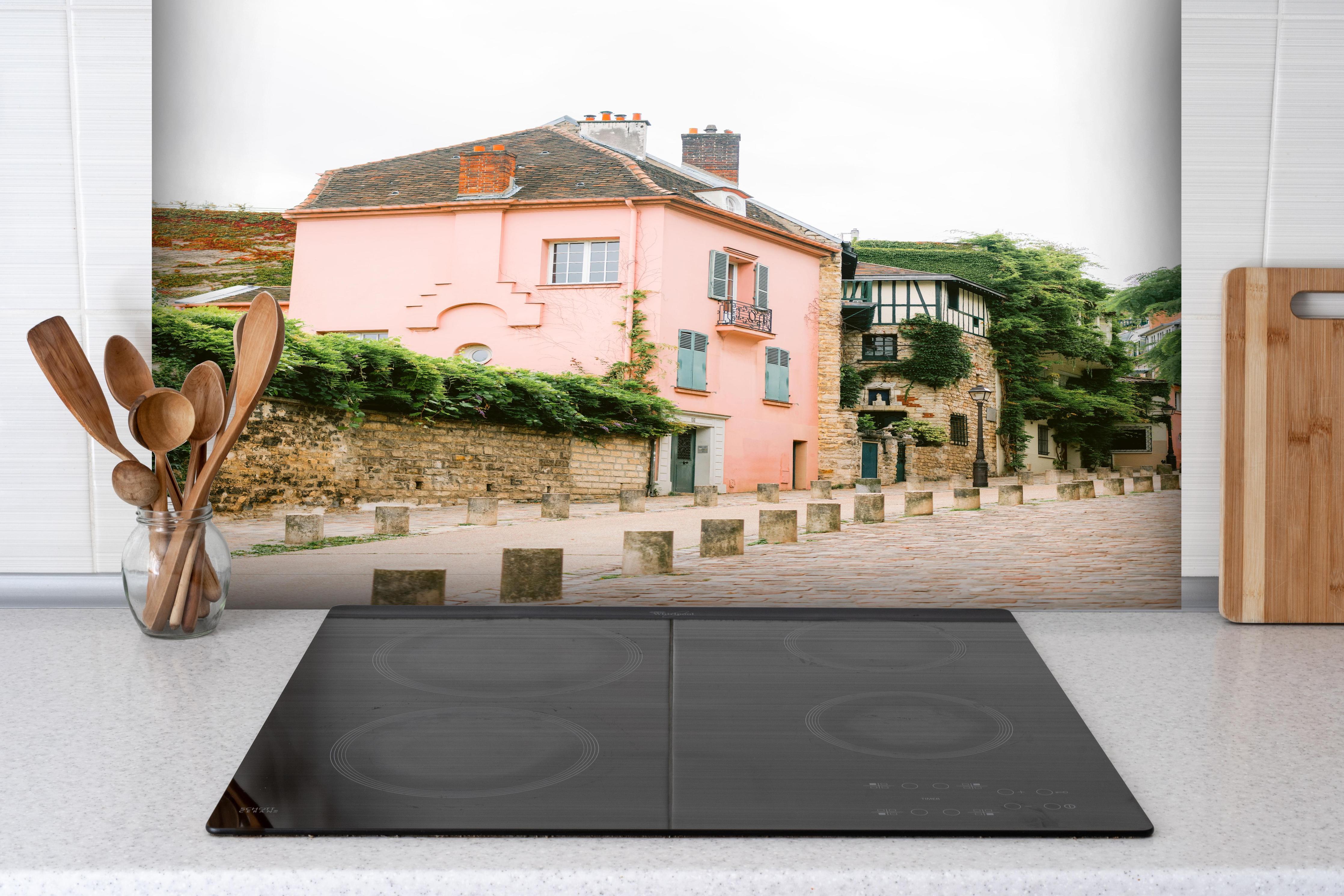 Spritzschutz - Charmantes Rosa Haus in Montmartre, Paris hinter einem Cerankochfeld zwischen Holz-Kochutensilien
