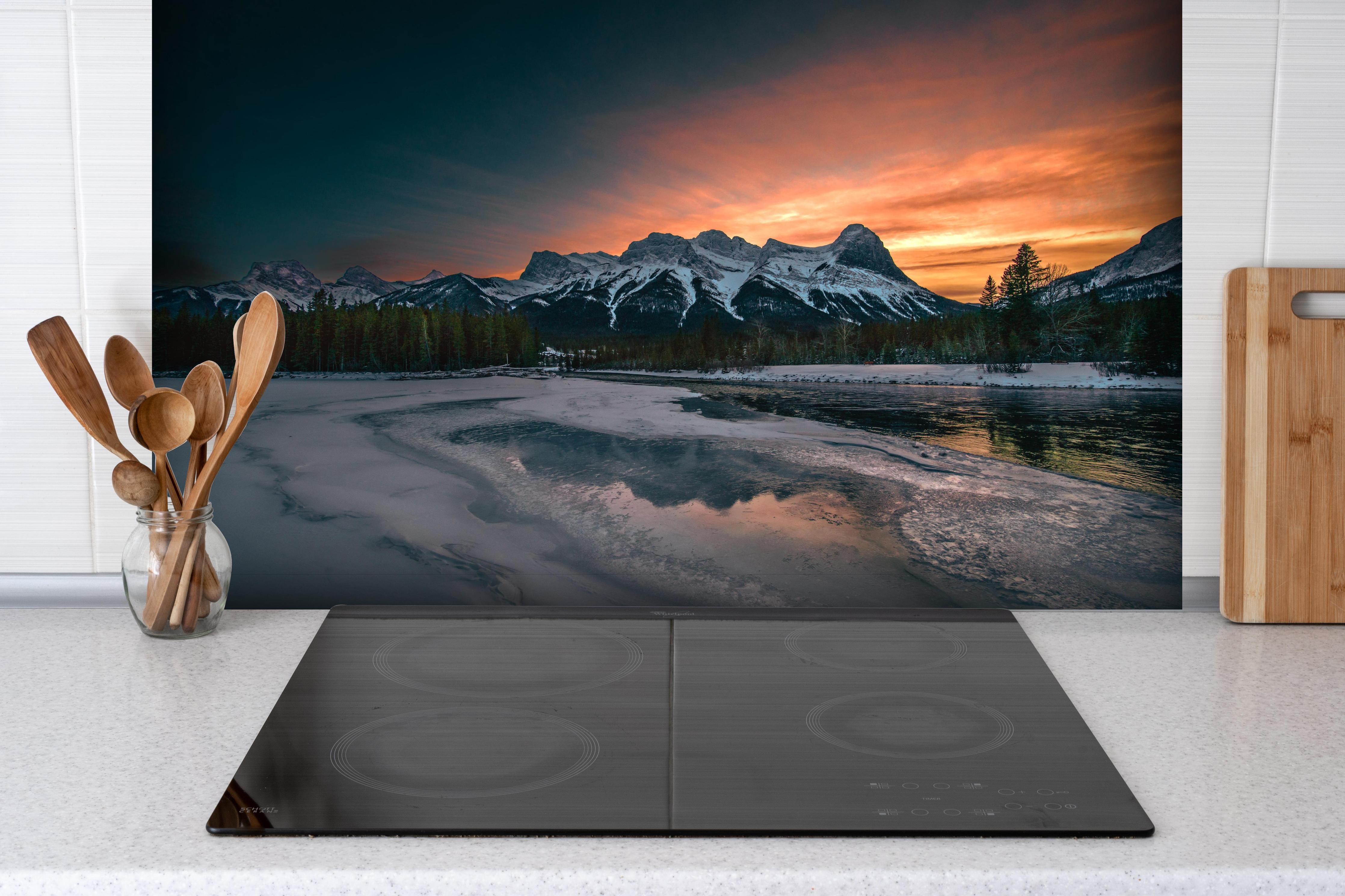 Spritzschutz - Dämmerung über schneebedeckten Bergspitzen hinter einem Cerankochfeld zwischen Holz-Kochutensilien
