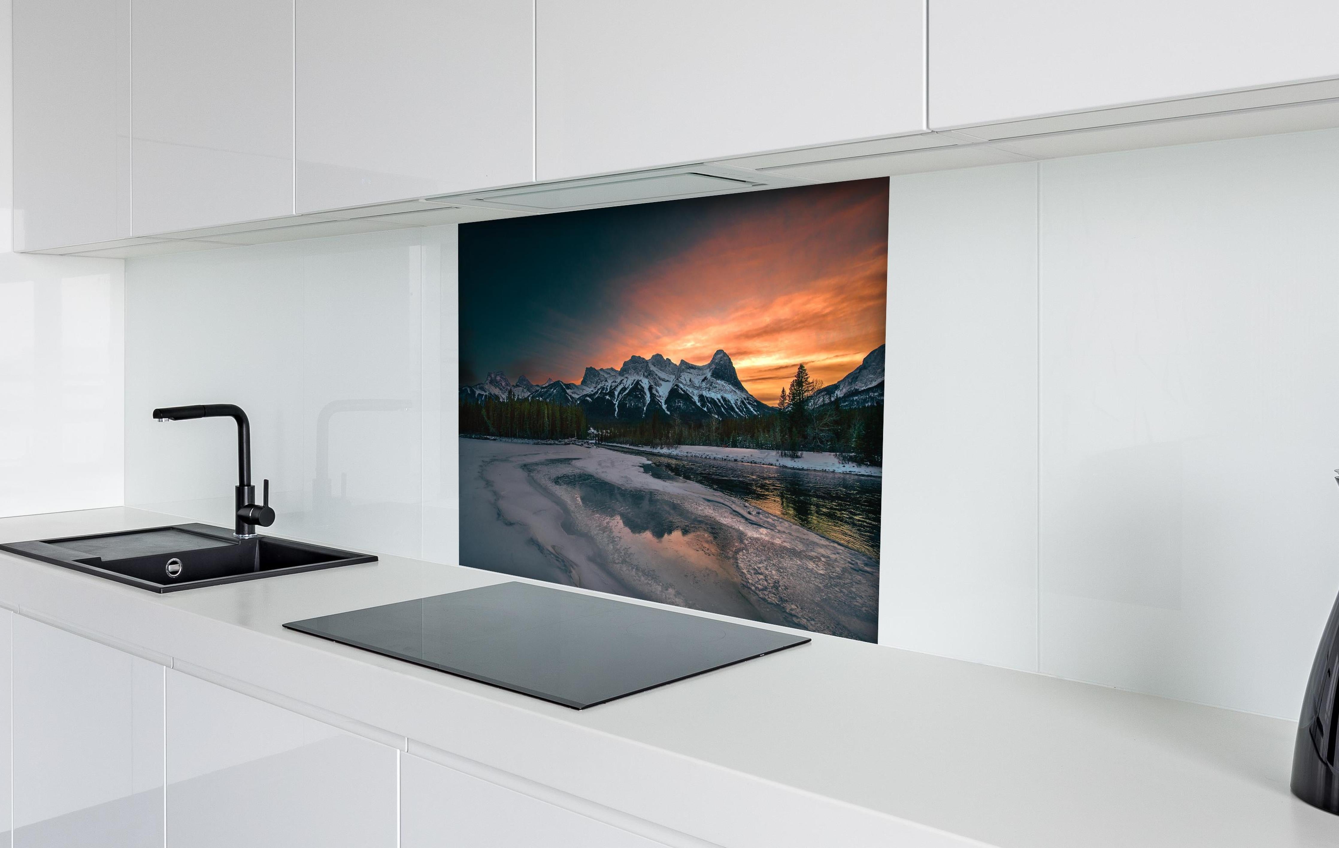 Spritzschutz - Dämmerung über schneebedeckten Bergspitzen hinter einem Cerankochfeld zwischen Holz-Kochutensilien
