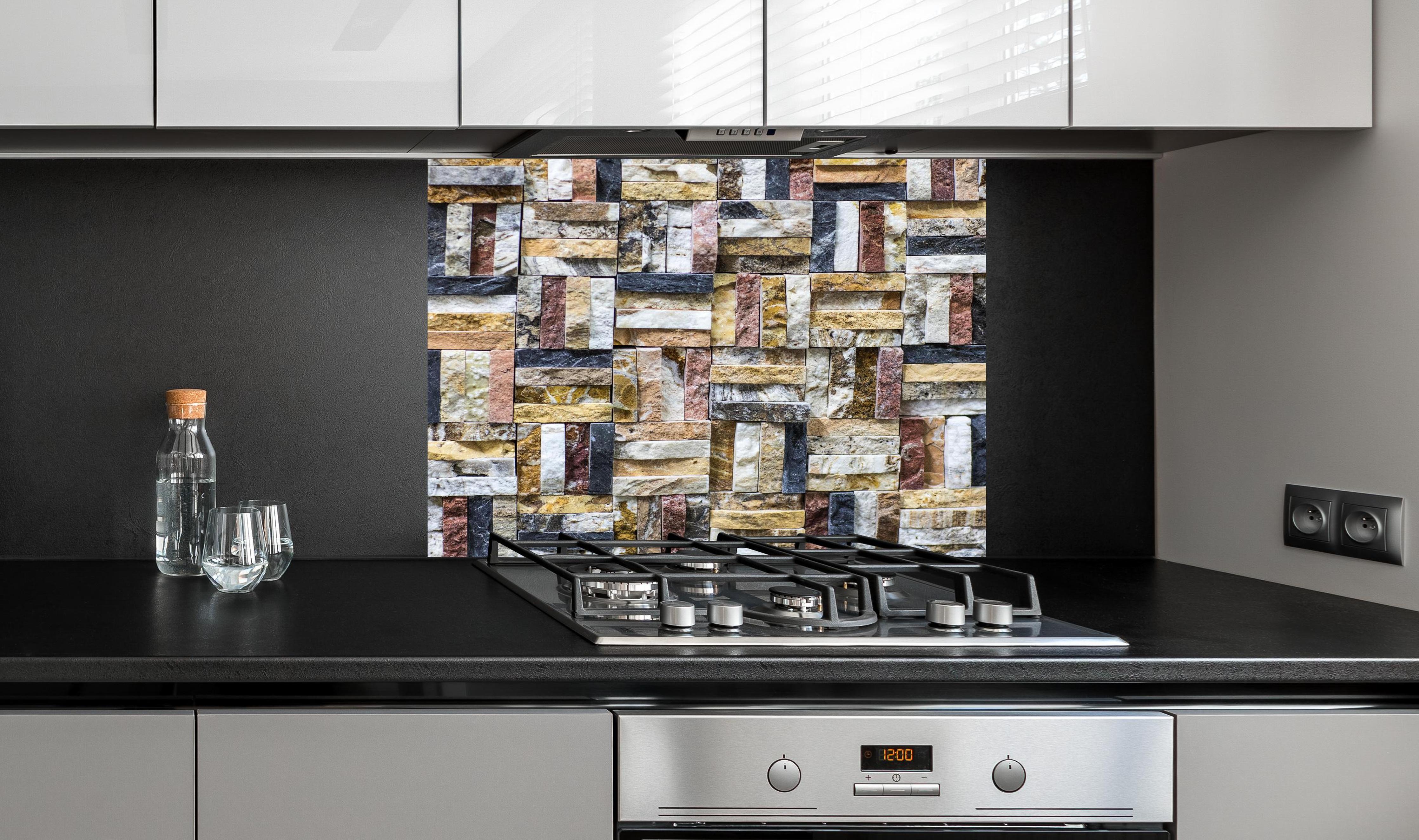 Spritzschutz - Dekoratives Wand Mosaik aus Naturstein hinter einem Cerankochfeld zwischen Holz-Kochutensilien
